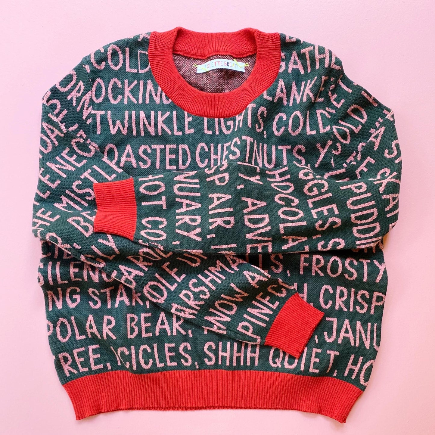 Knitted holiday sweater with festive christmas text pattern on a pink background