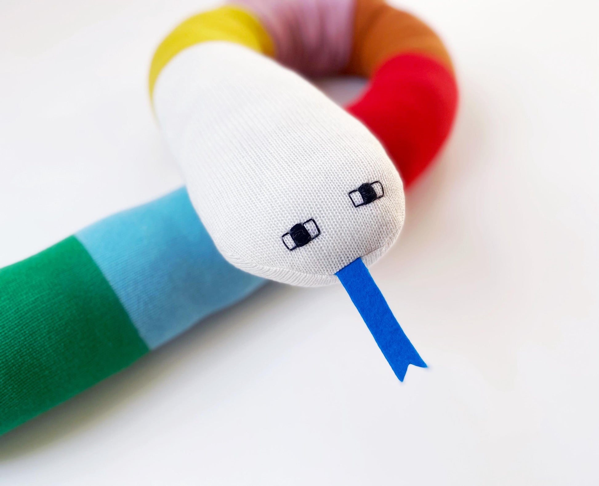 Colorful knitted toy snake with a white face on a light background
