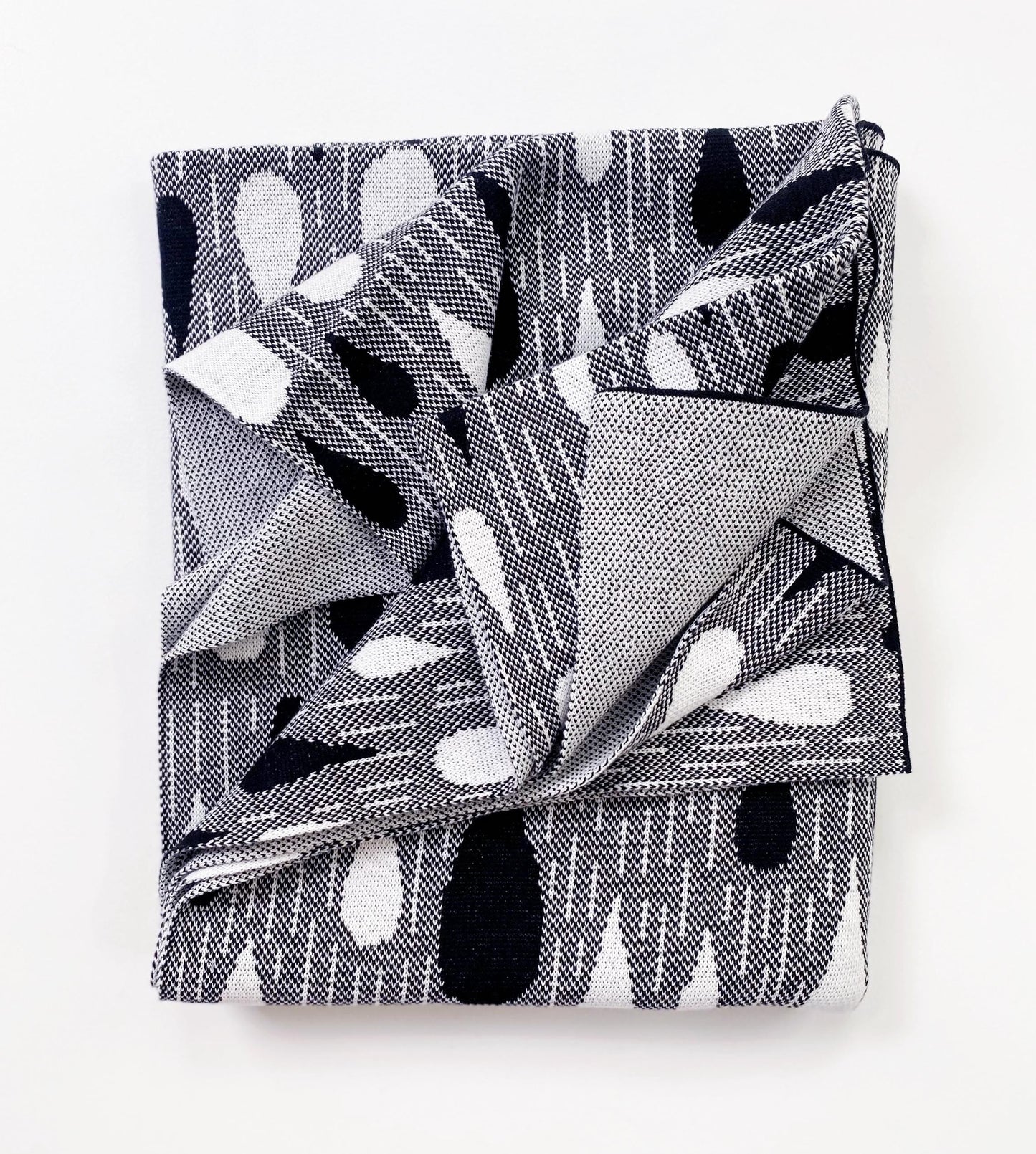 Folded knitted blanket throw with black and white raindrop pattern on a white background