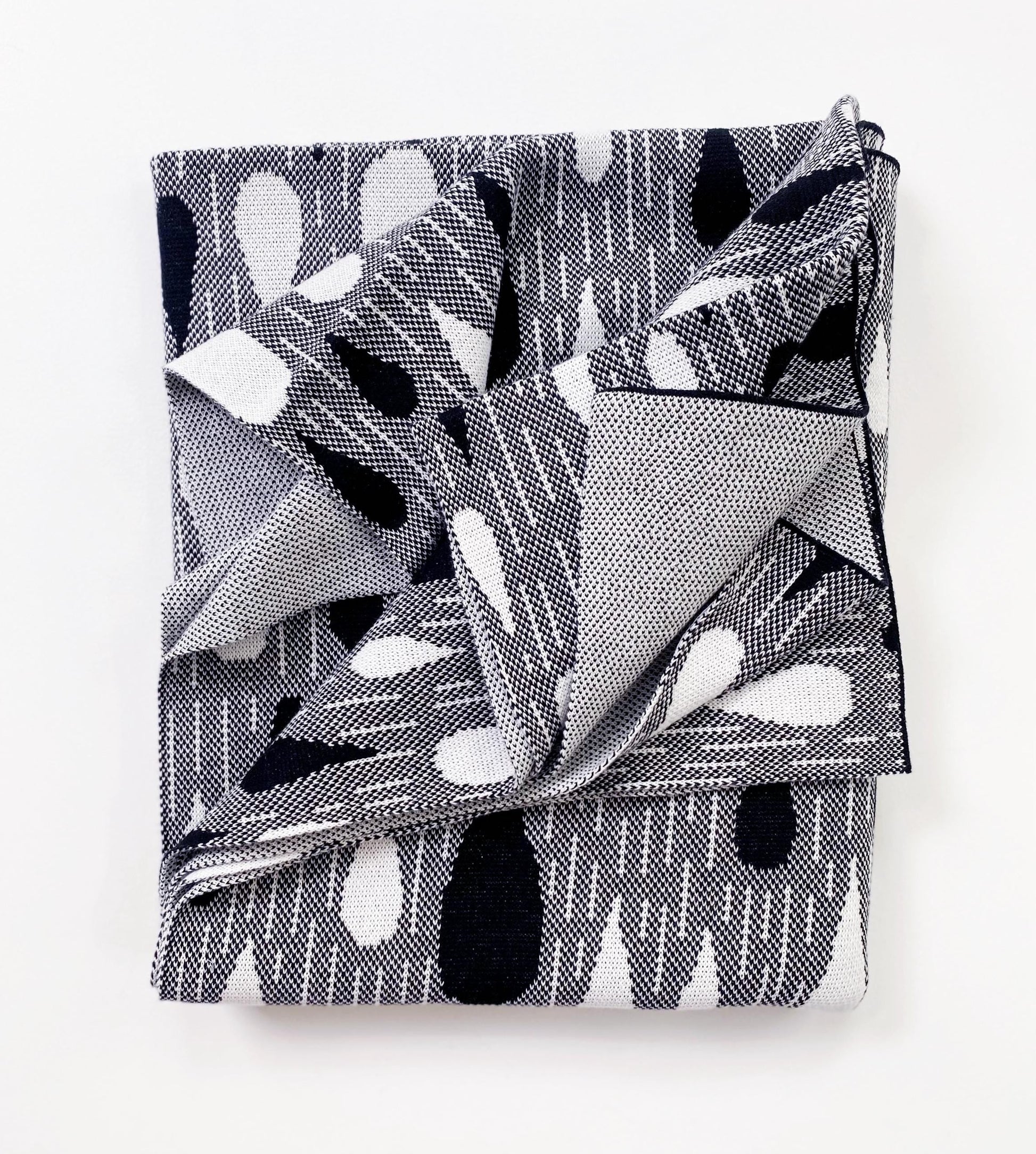 Folded knitted blanket throw with black and white raindrop pattern on a white background