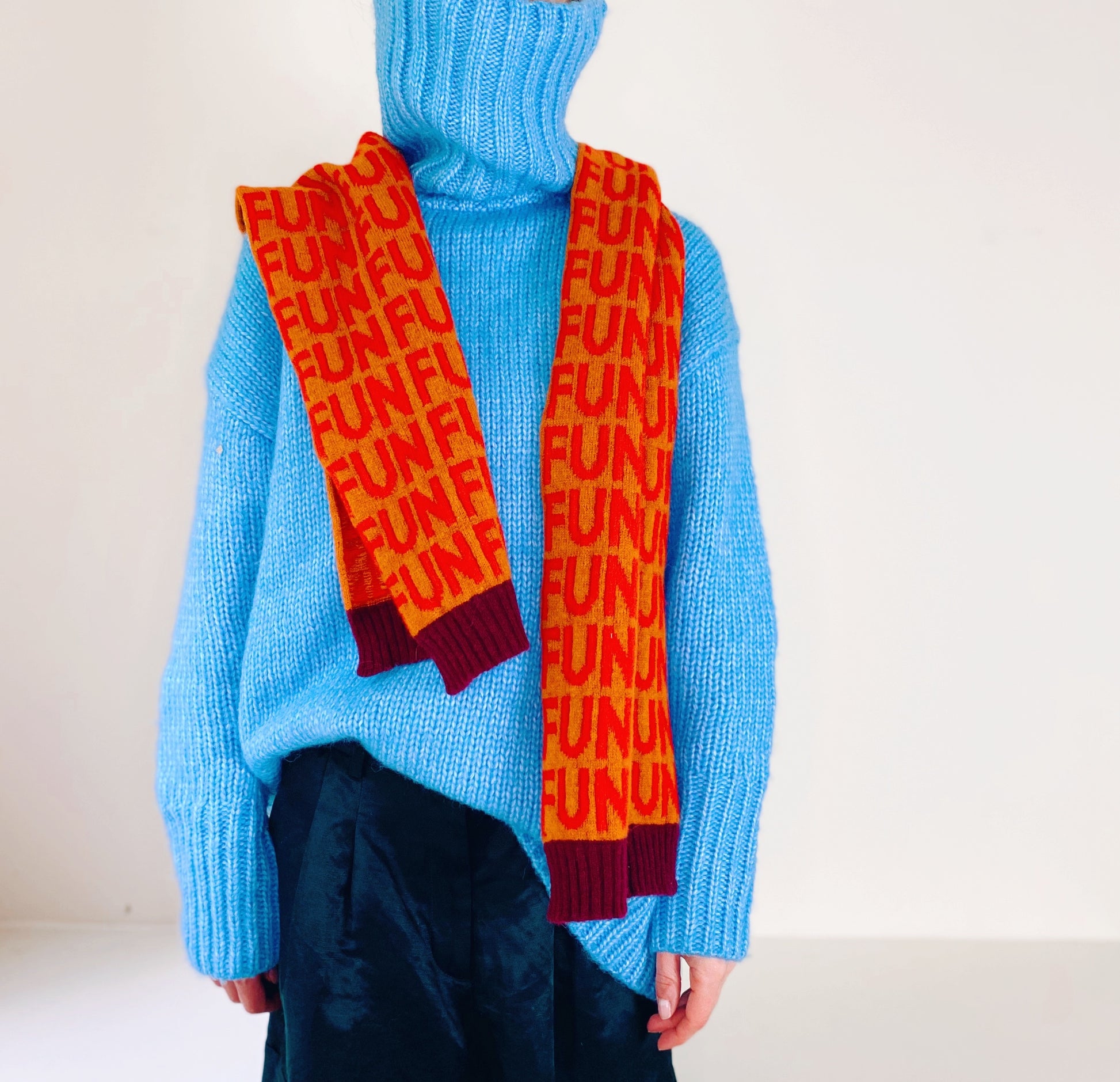 Person wearing a blue sweater and orange scarf with 'FUN' pattern on a plain background