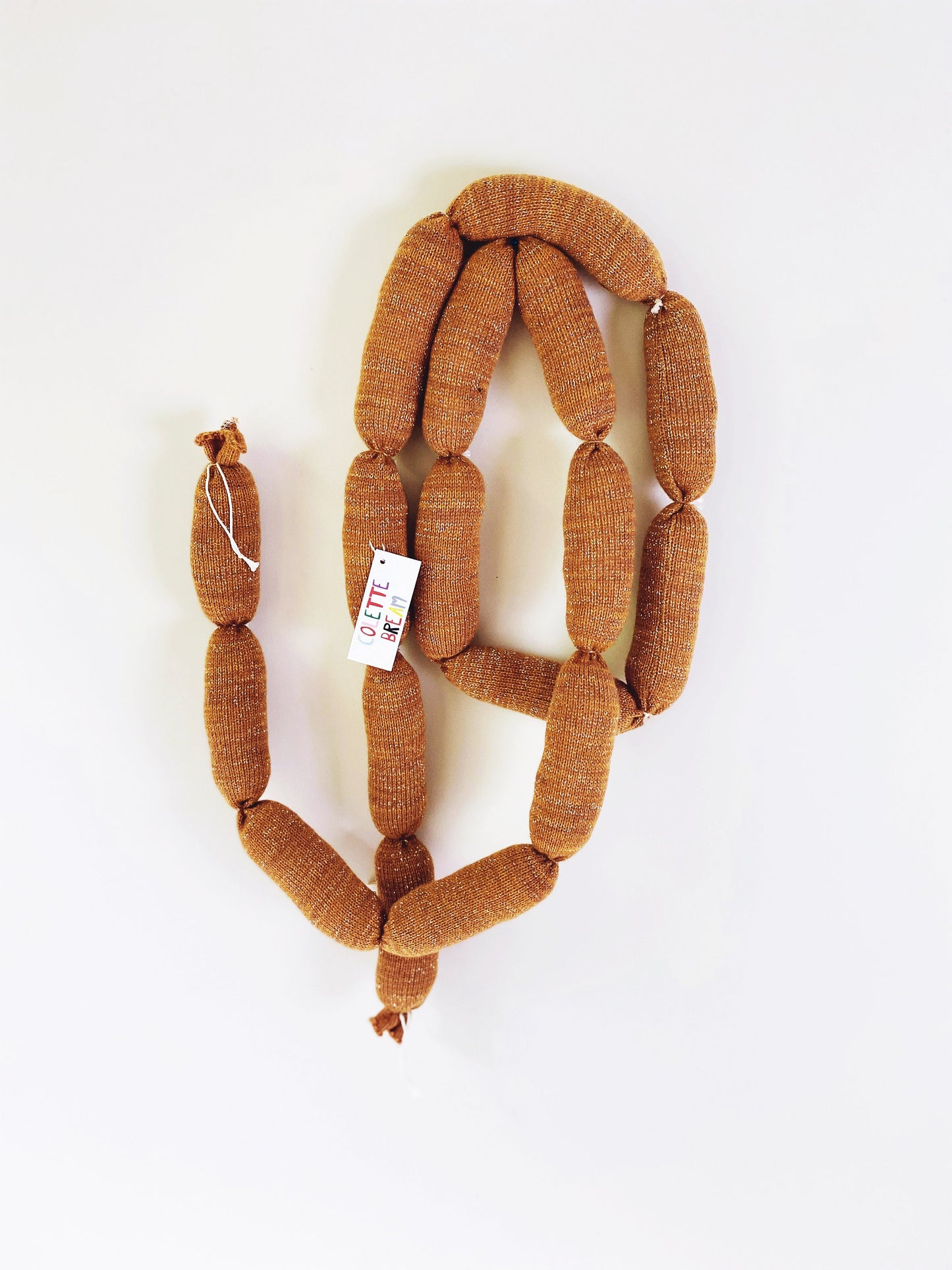 Brown knitted sausage links with a tag on a white background