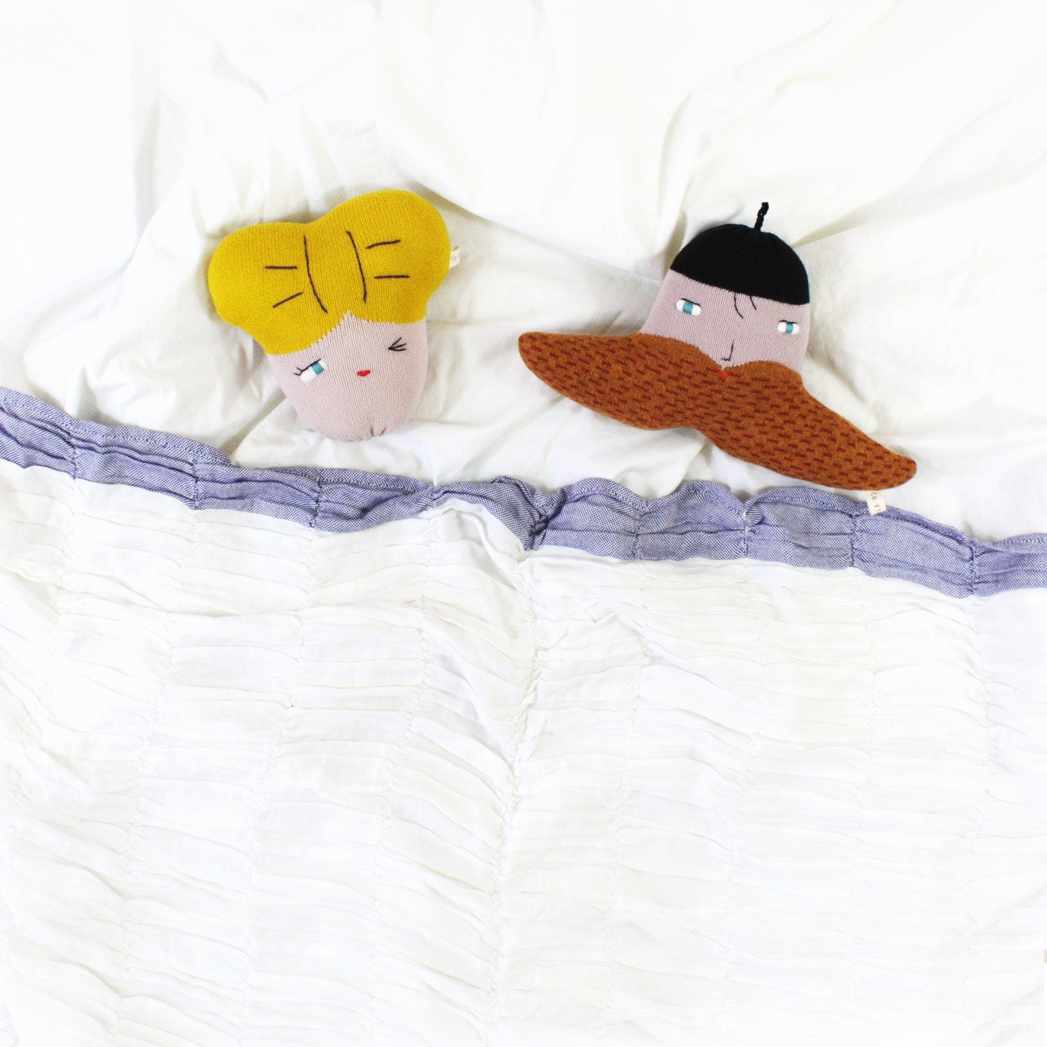Two plush toys, one with yellow hair and the other with a black hat and brown mustache, lying on a white surface.