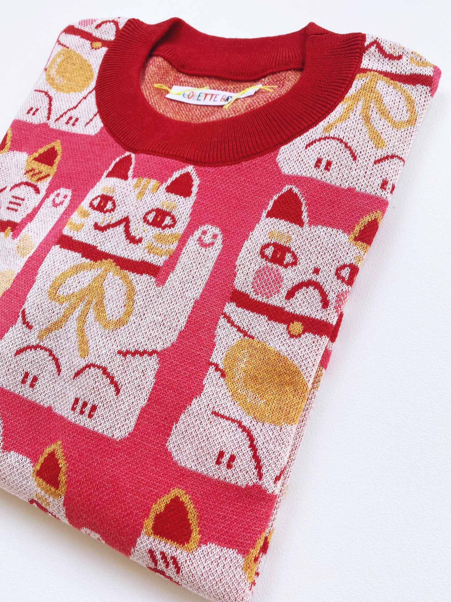 Pink sweater with maneki neko cat pattern on a white background
