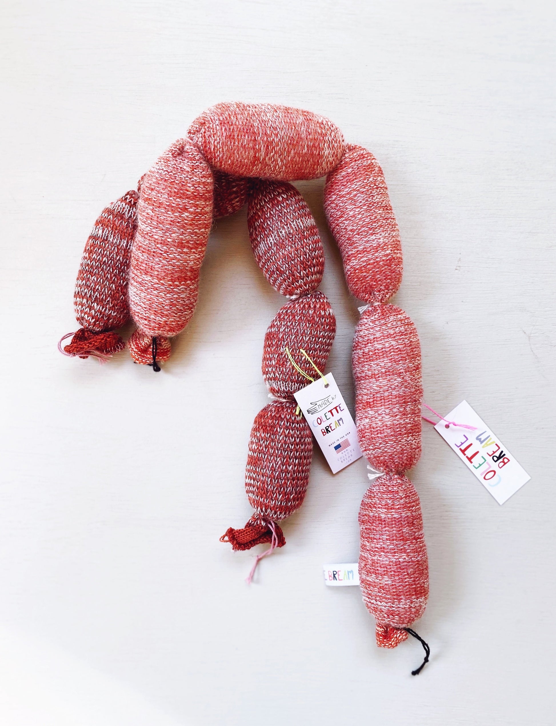 A pair of handmade knitted lambswool sausages with tags on a white background