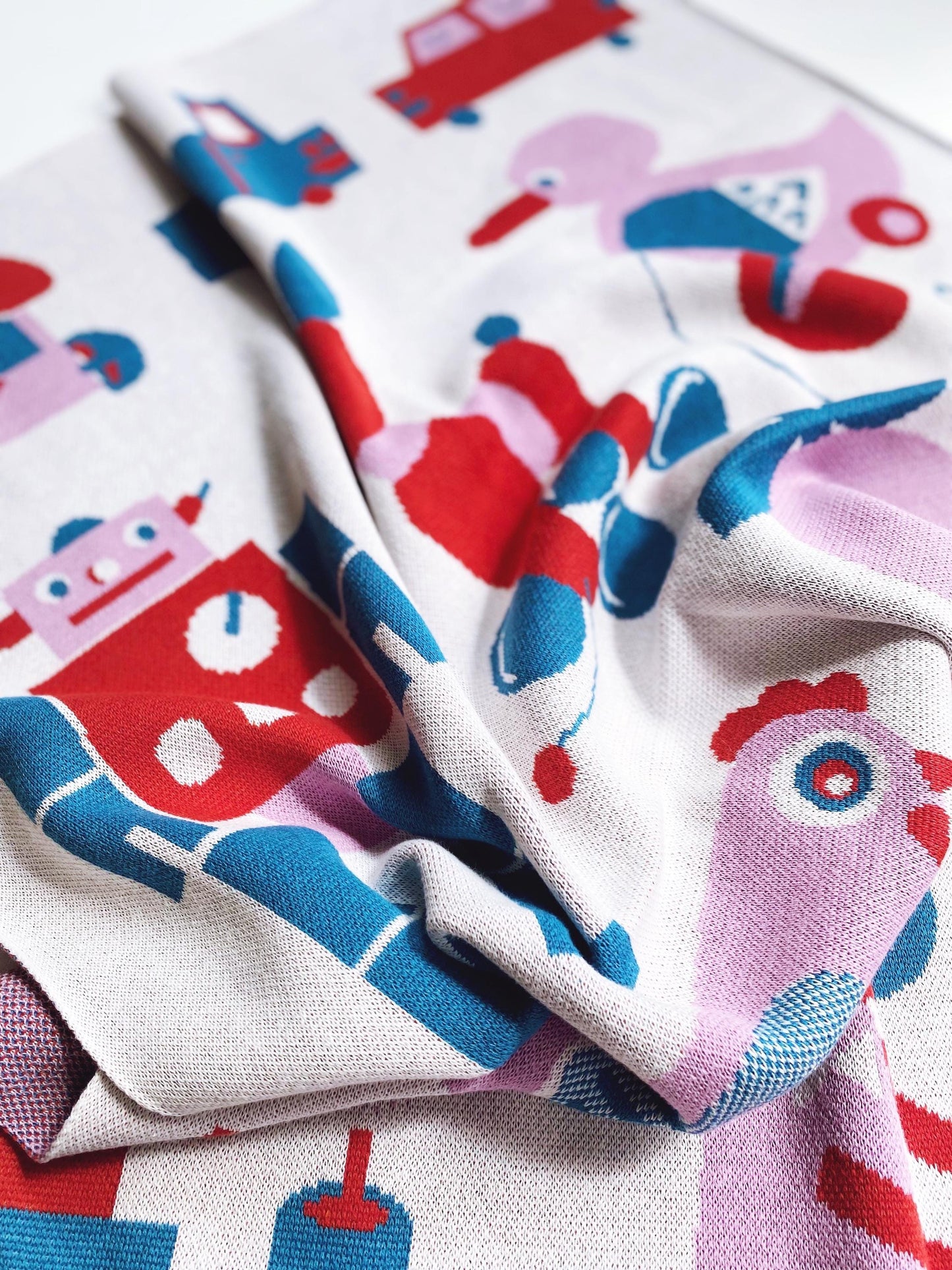 Colorful knit blanket fabric with cartoon characters including robots and cars on a white background