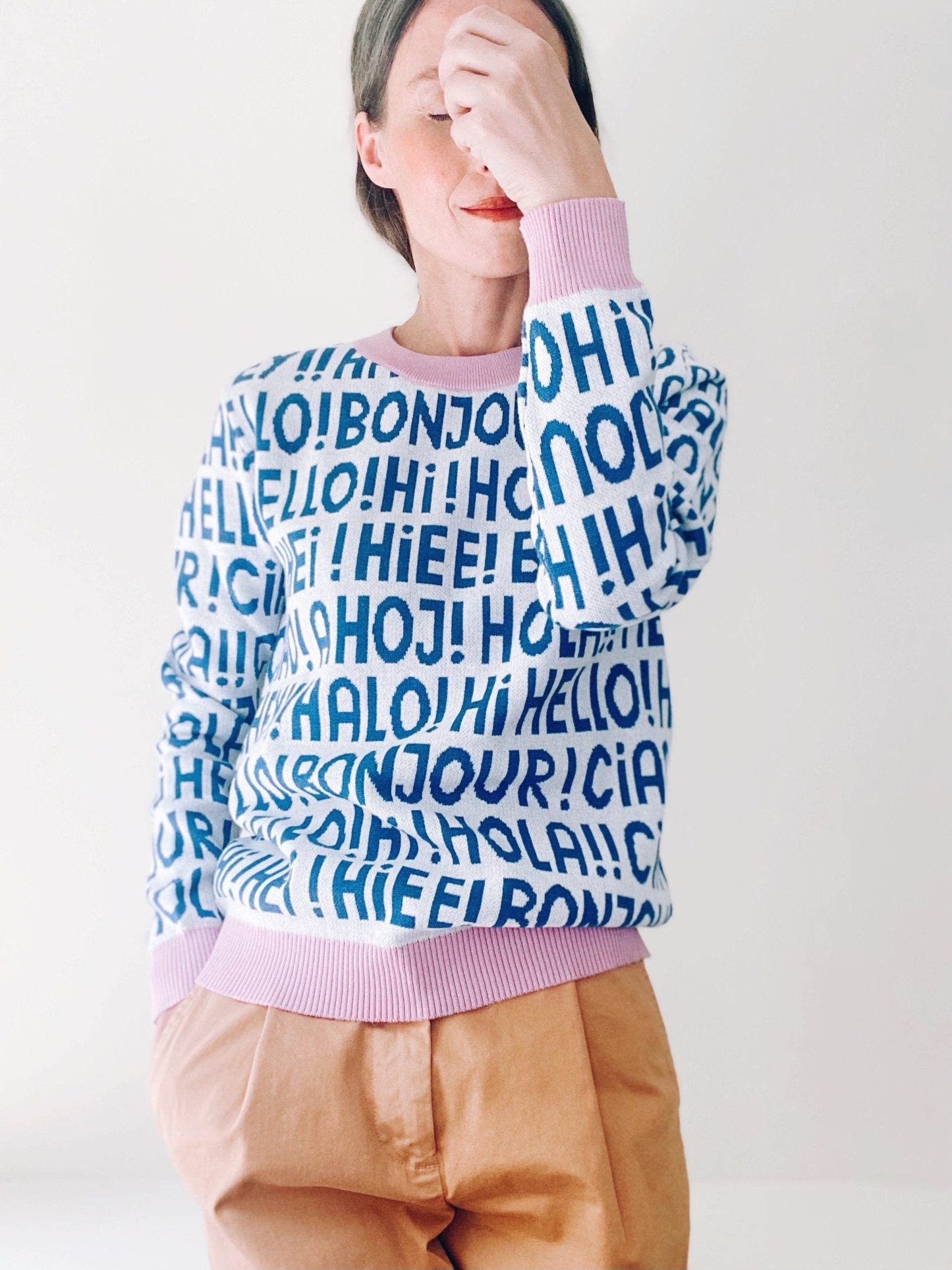 Person wearing a colorful sweater with greetings text patterns on a plain background