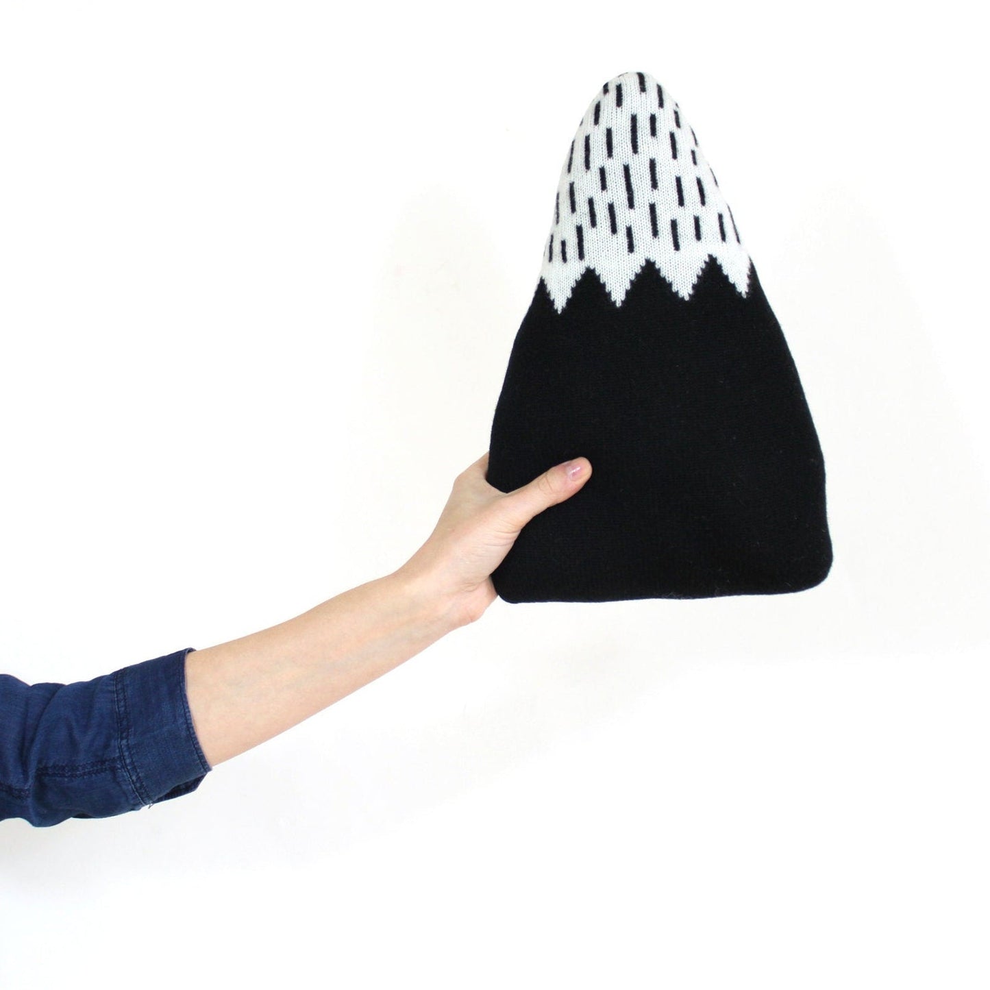 Black and white patterned mountain shaped knitted pillow held by a hand on a white background