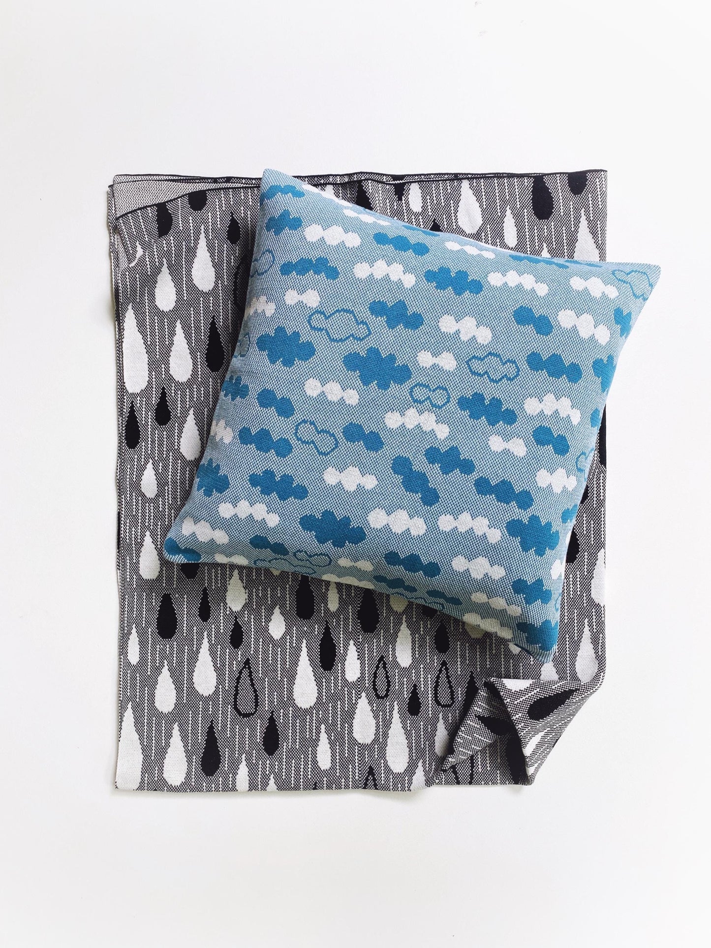 Blue knitted pillow with cloud pattern on a gray blanket with raindrop pattern