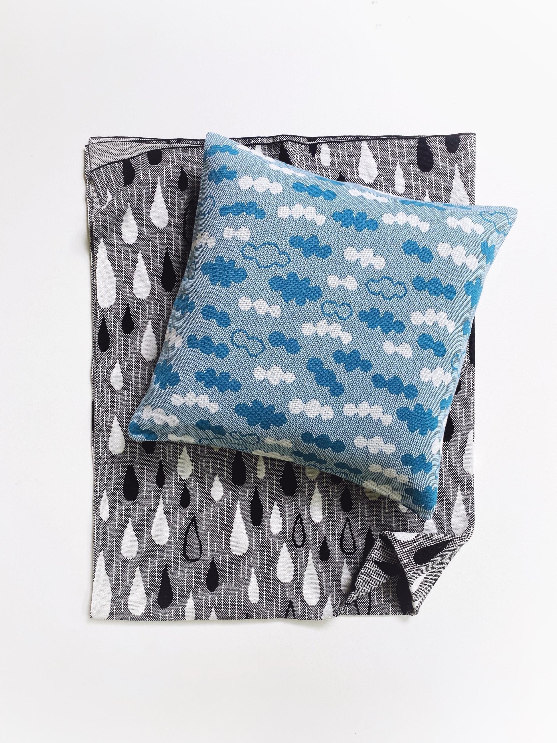Blue knitted pillow with cloud pattern on a gray blanket with raindrop pattern