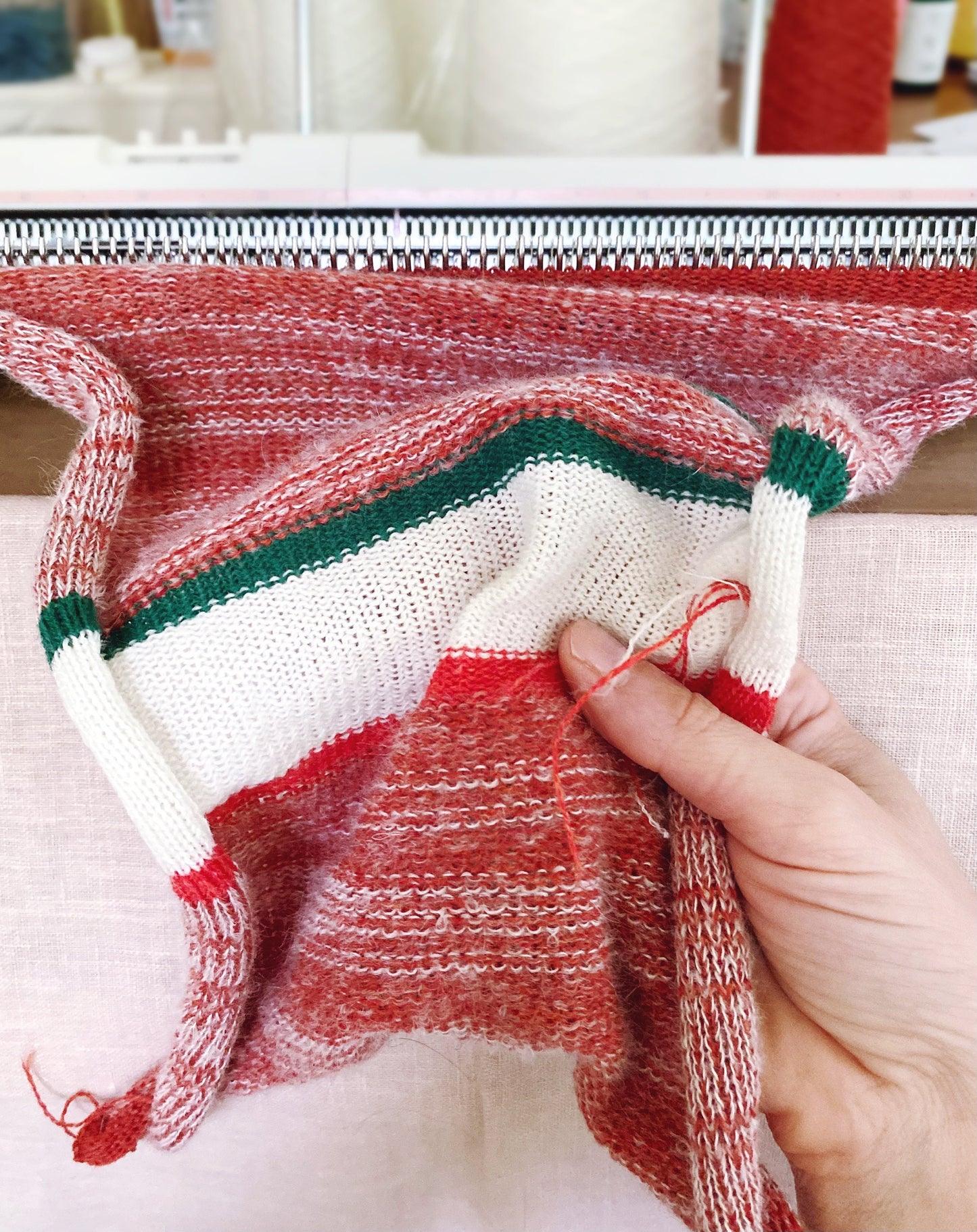 Hand knitting a red, white, and green fabric with a blurred background