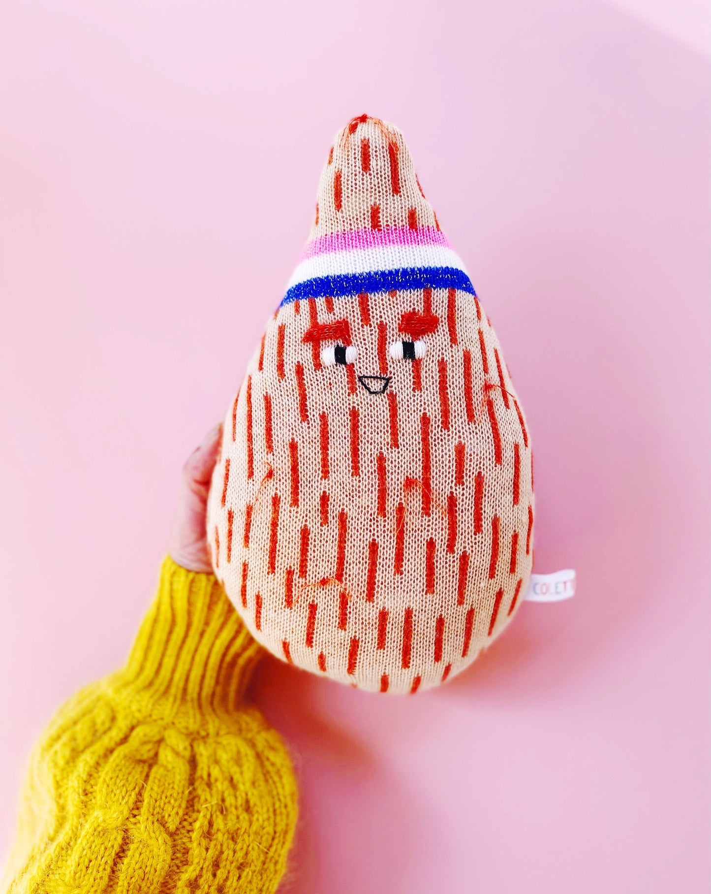 Knitted coconut plush toy with a face on a pink background