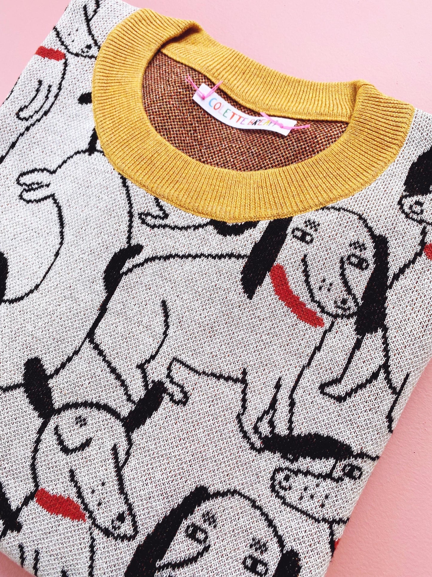 Close-up of a sweater with cartoon dachshund dog pattern and yellow neckline on a pink background