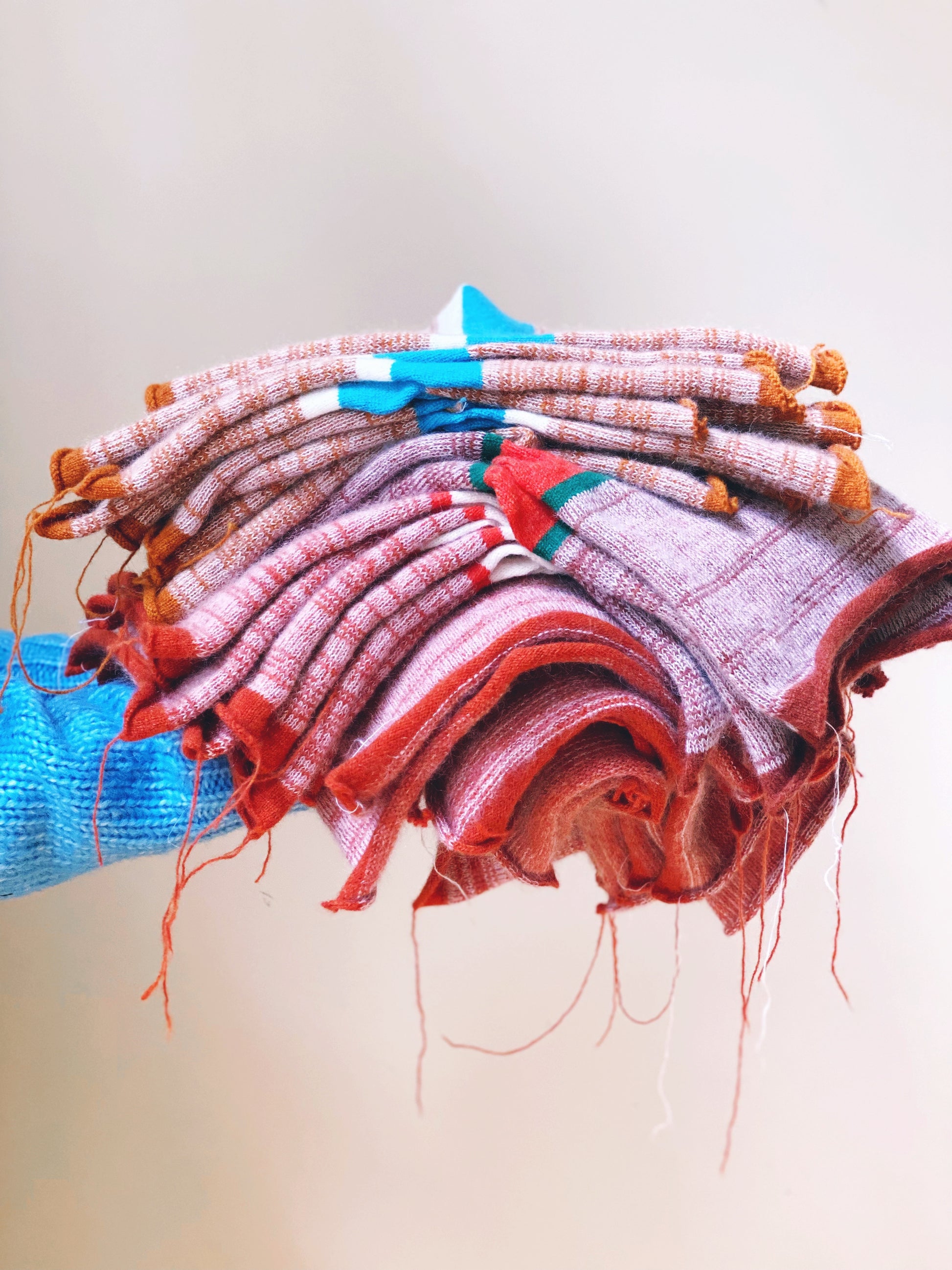 Stack of colorful knitted fabrics with a blue object underneath on a light background