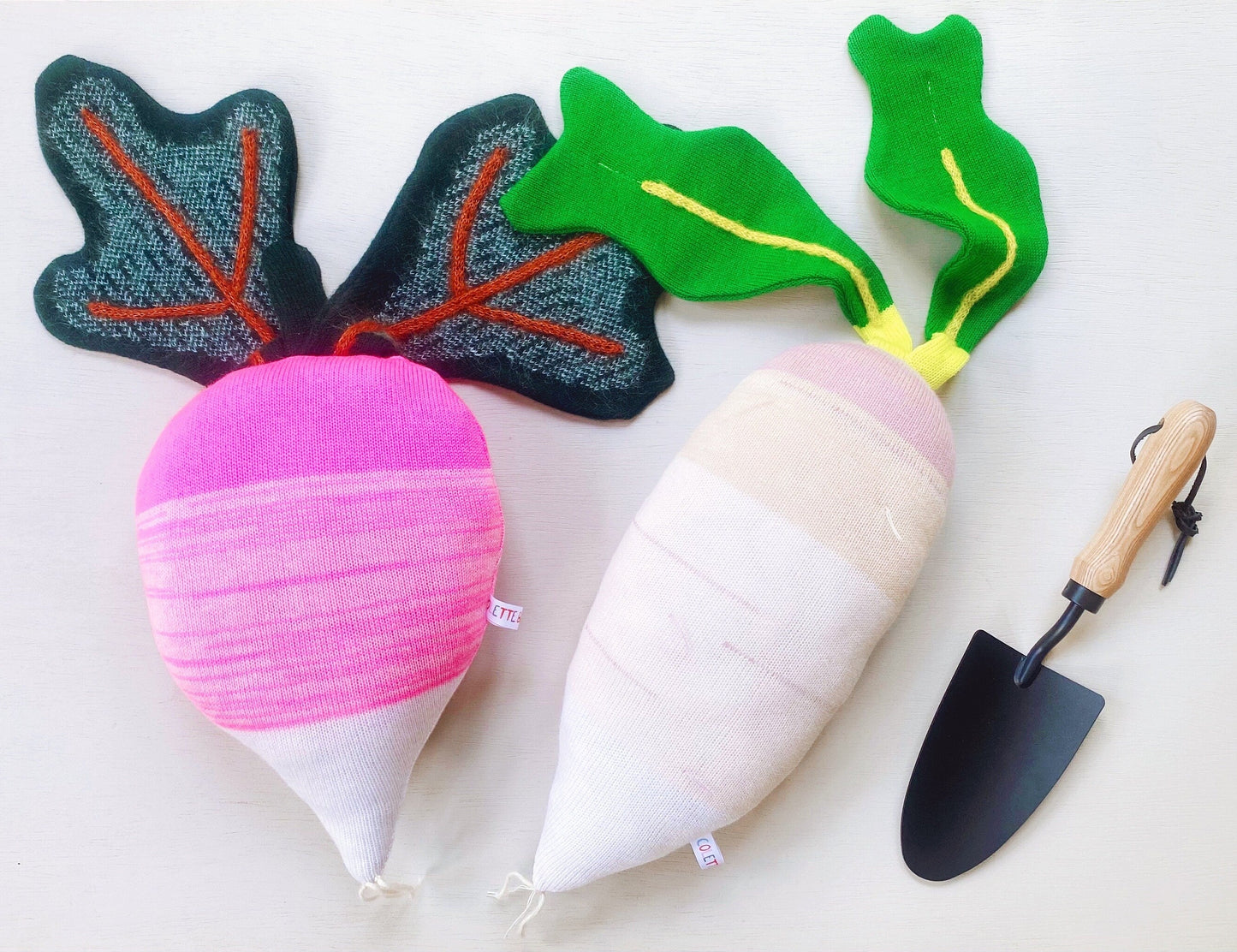 Plush radish toys and pillows with leafy greens and a small showel on a light background