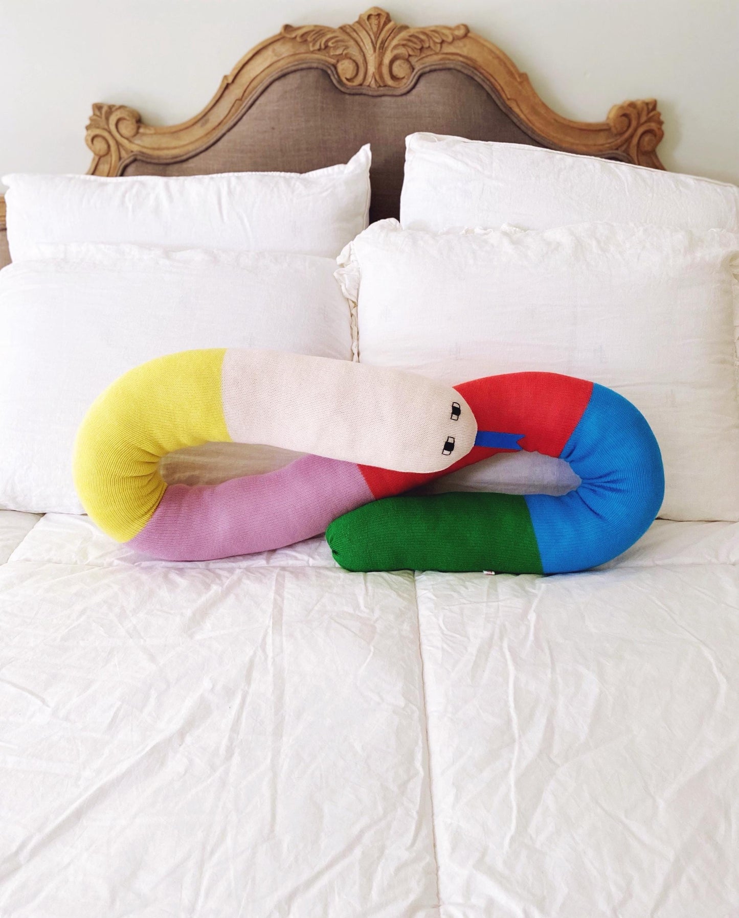 Colorful snake-shaped pillow on a bed with white pillows and a wooden headboard.