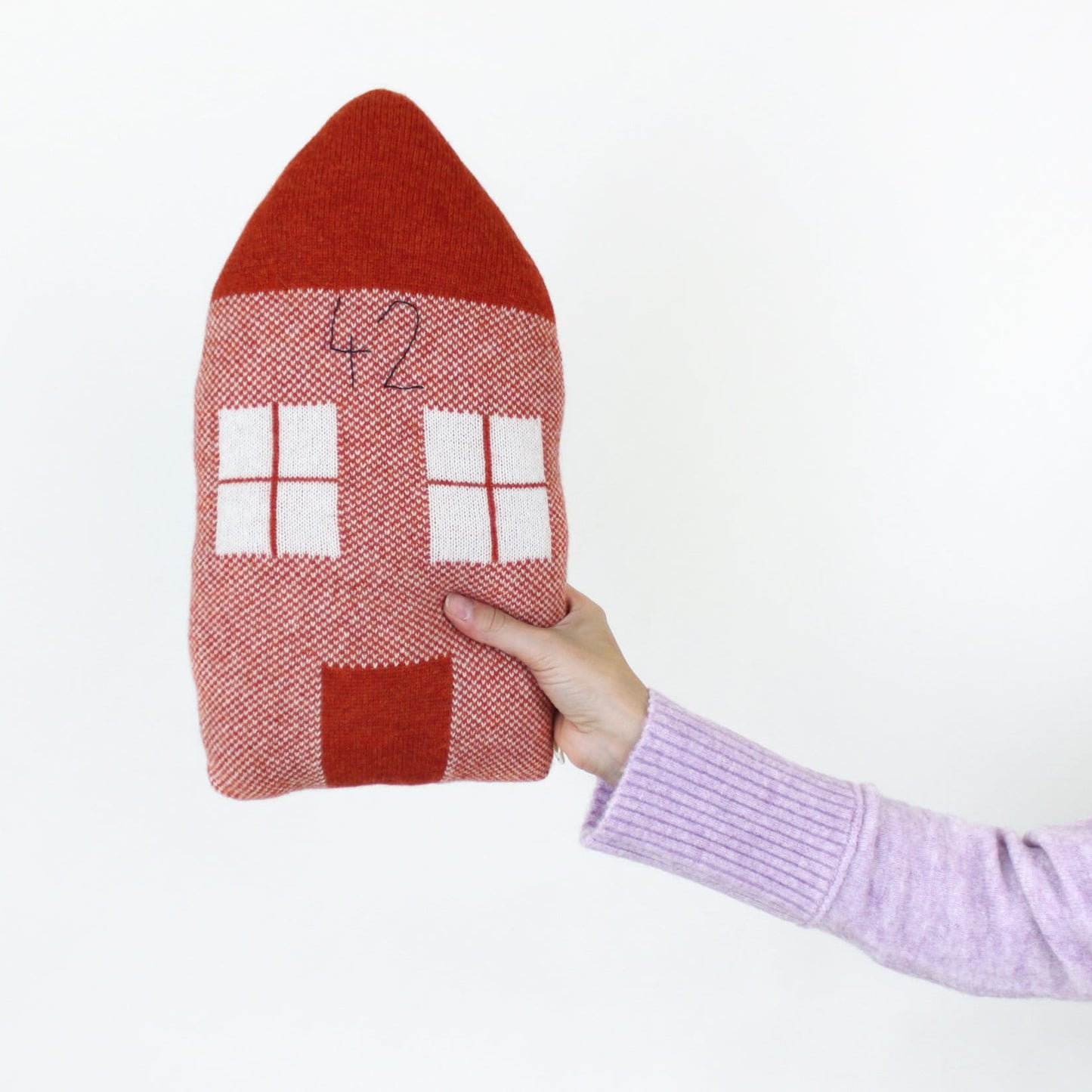 Hand holding a knitted house-shaped cushion with a number on a white background