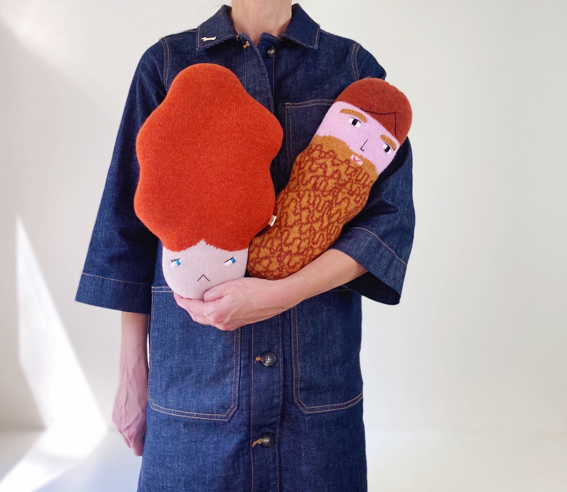 Person holding two plush toys resembling a face with a beard on a plain background