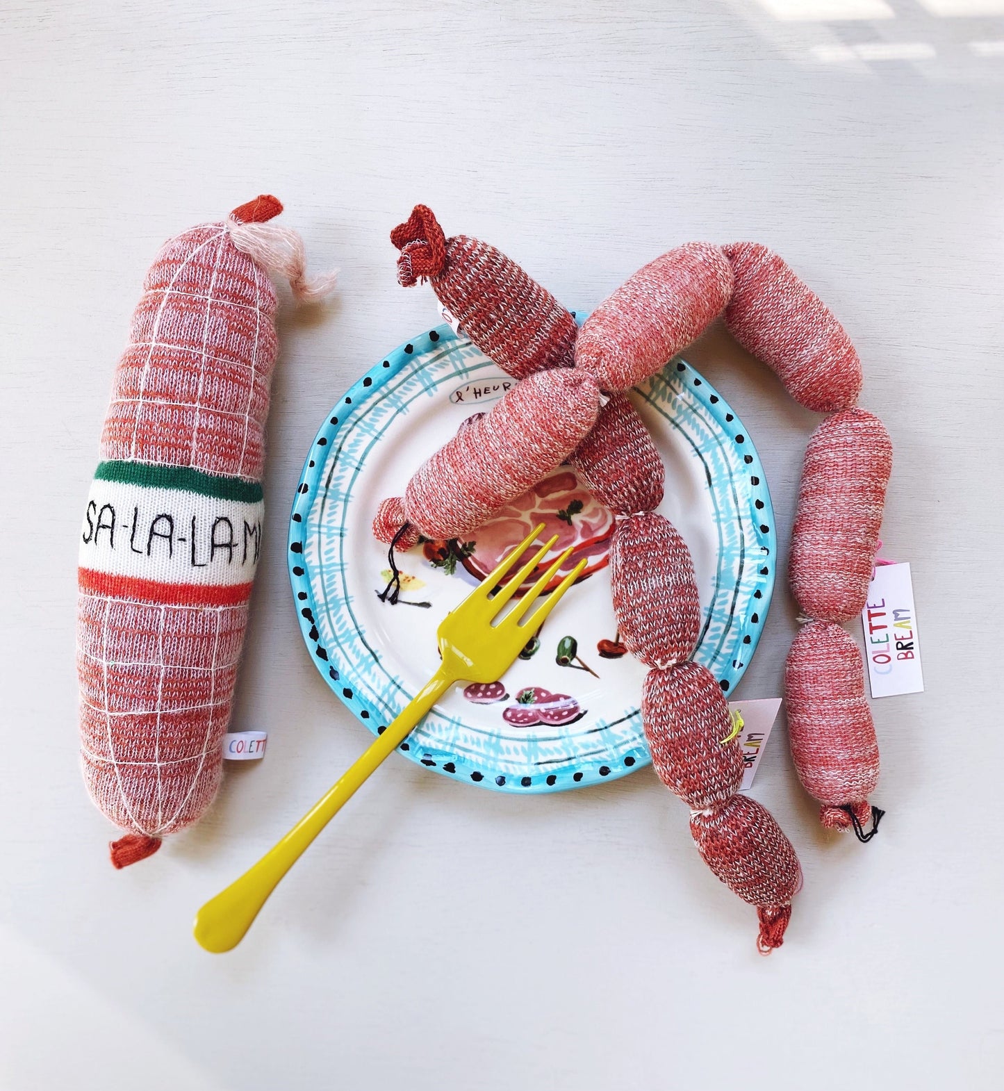 Knitted sausages and salami plate with a yellow fork on a white background
