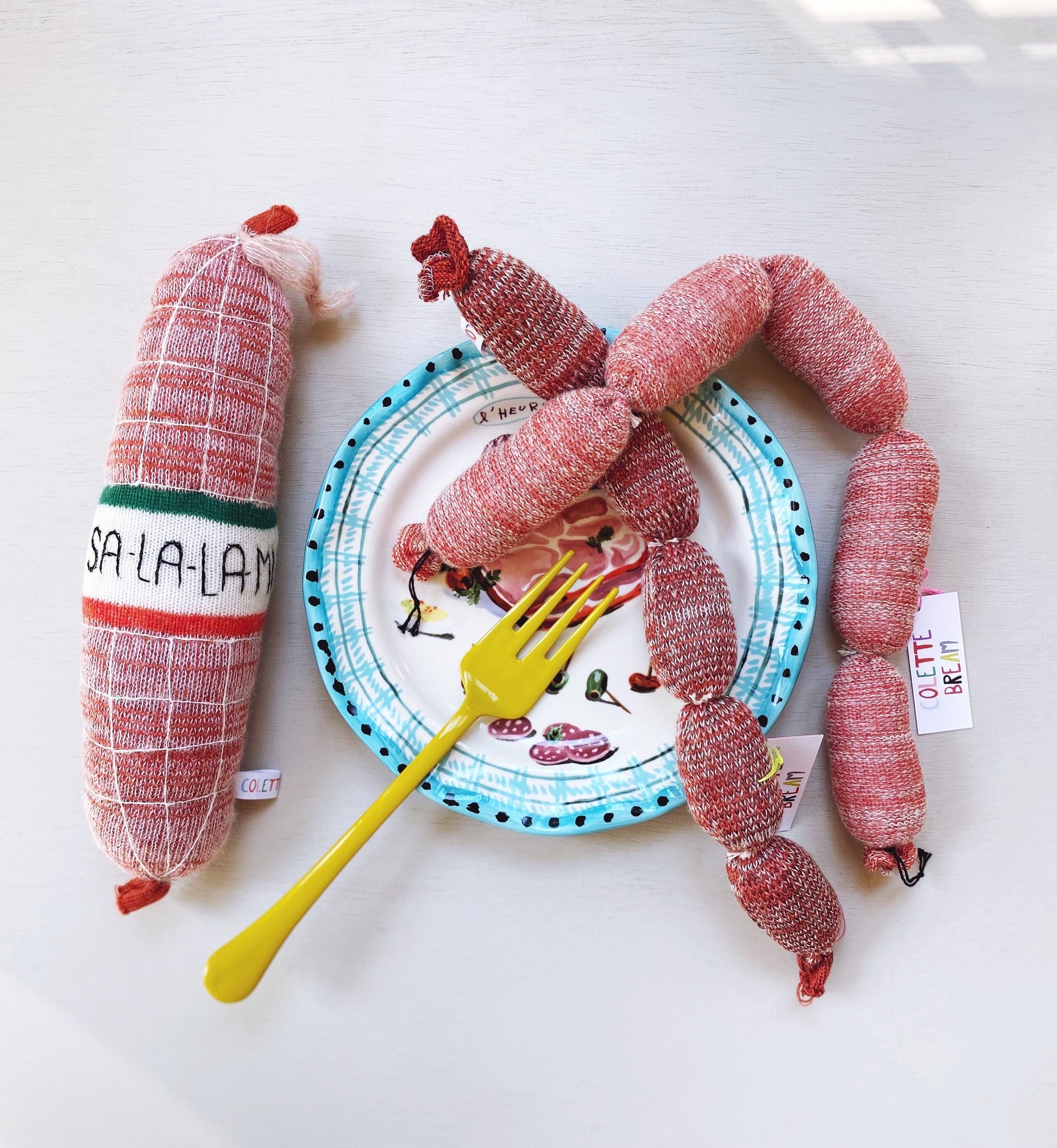 Knitted sausages and salami plate with a yellow fork on a white background