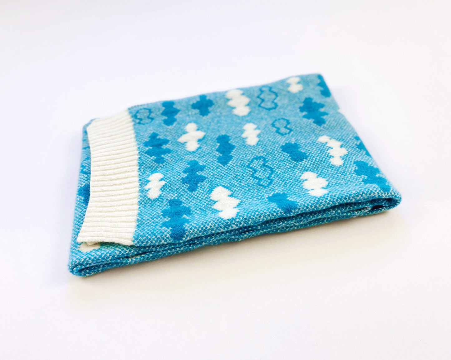 Folded blue knitted scarf with white and blue cloud patterns on a white background