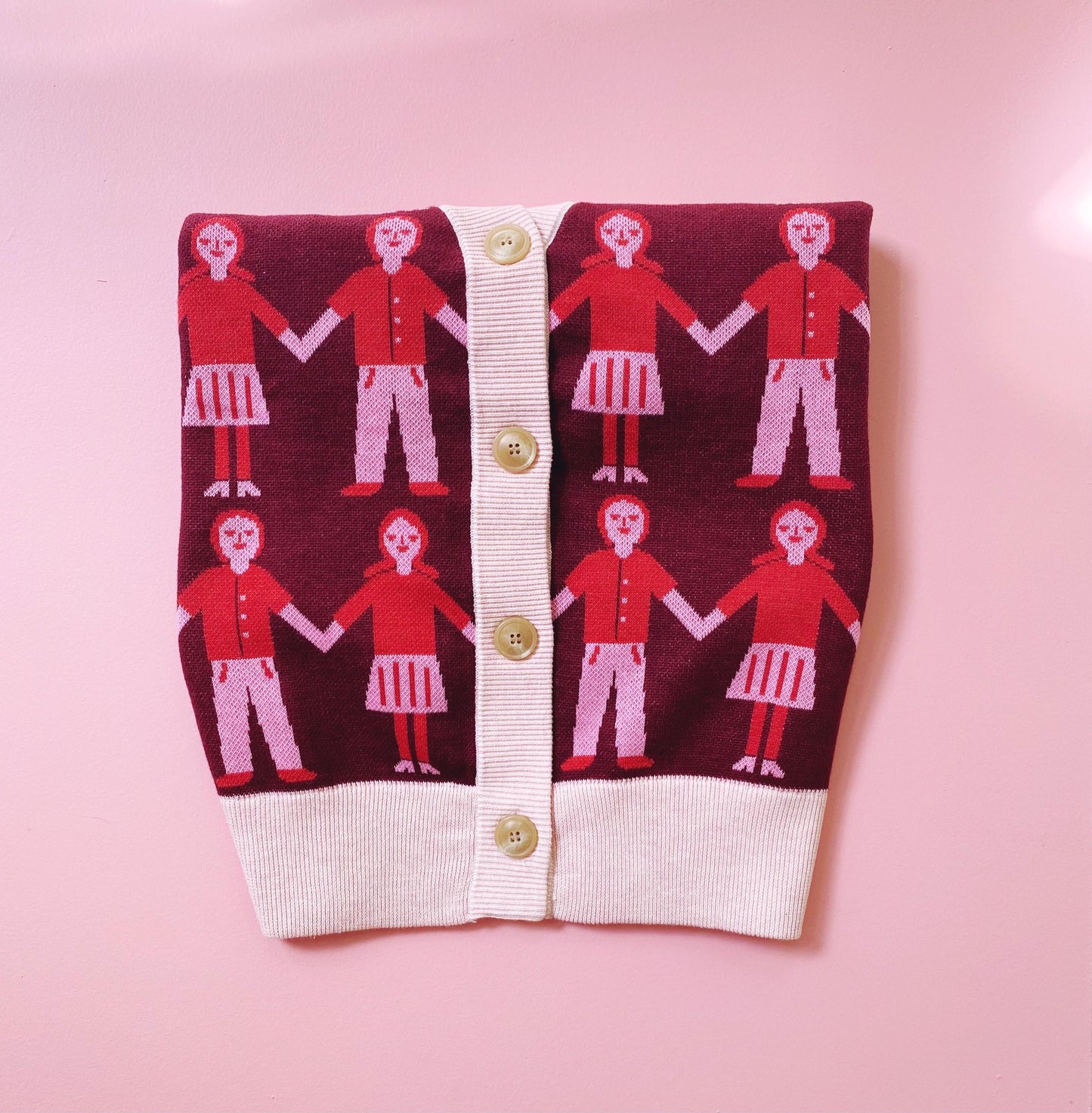 Knitted cardigan with red and white pattern of people holding hands on a pink background