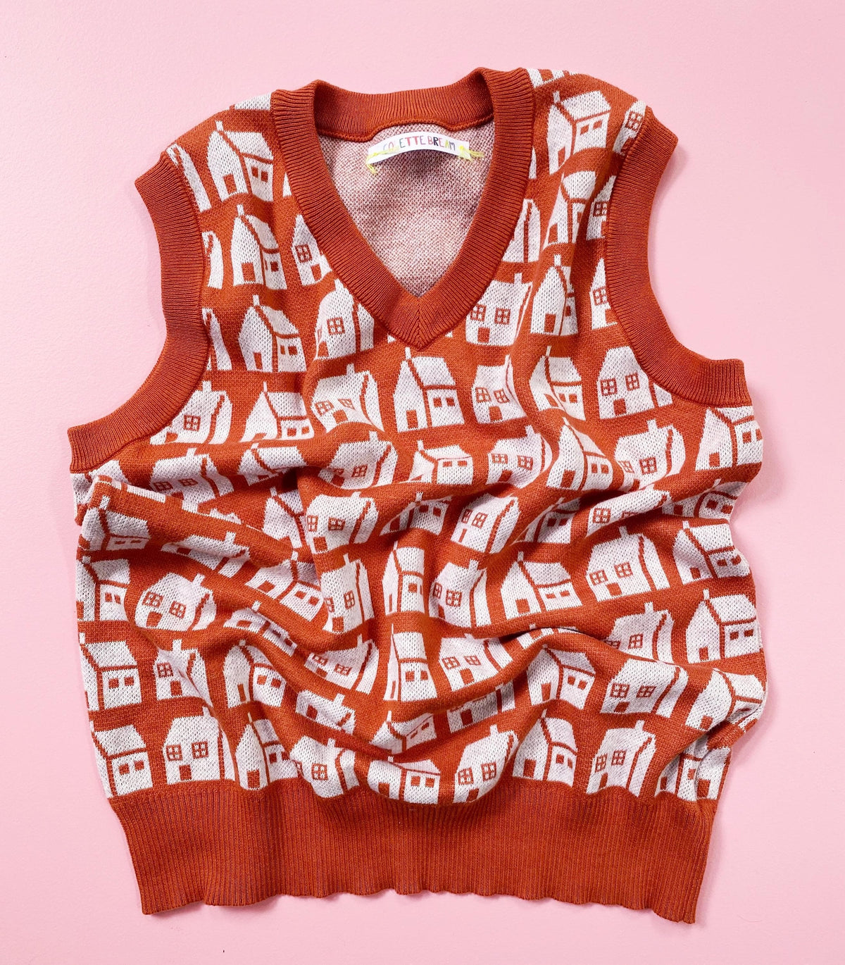 Orange knit sleeveless sweater vest with house pattern on a pink background
