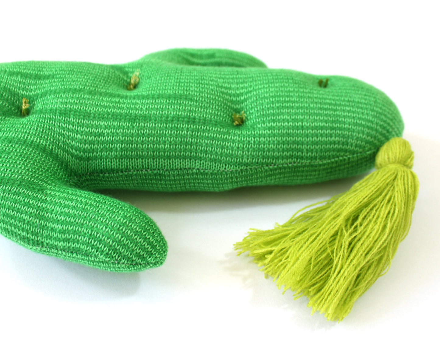 Green knitted toy resembling a cactus with tassel on a white background