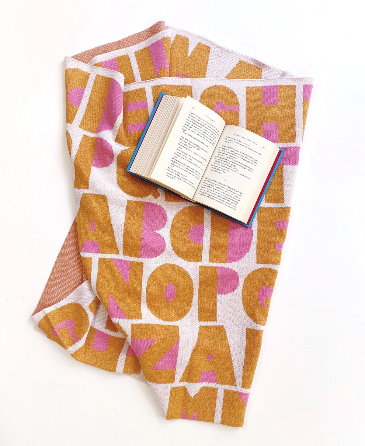 Textile with a colorful letter pattern draped over an open book on a white background