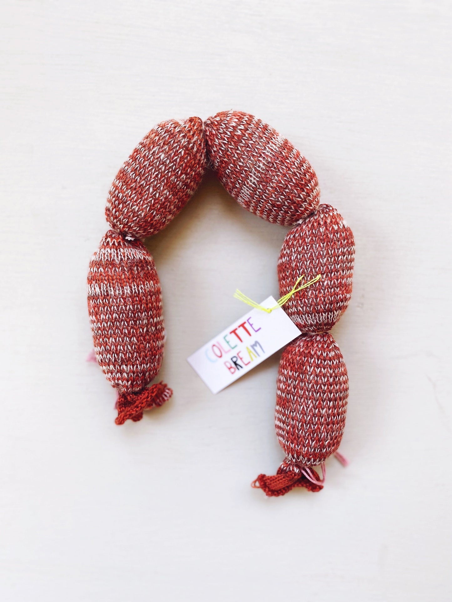 Red and brown knitted sausage with a visible brand tag on a white background
