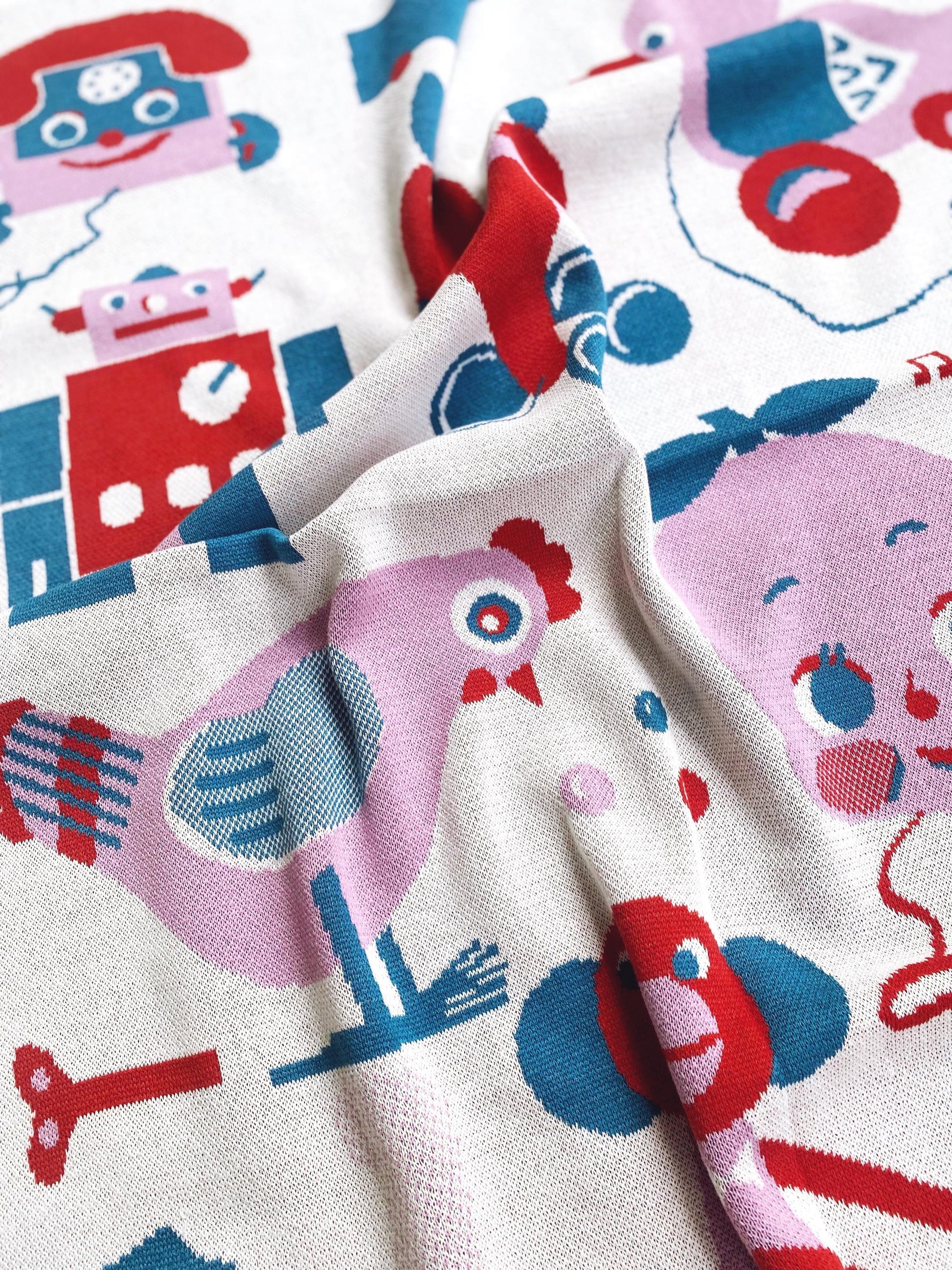 Close-up of a knitted blanket fabric with colorful robot and animal patterns.