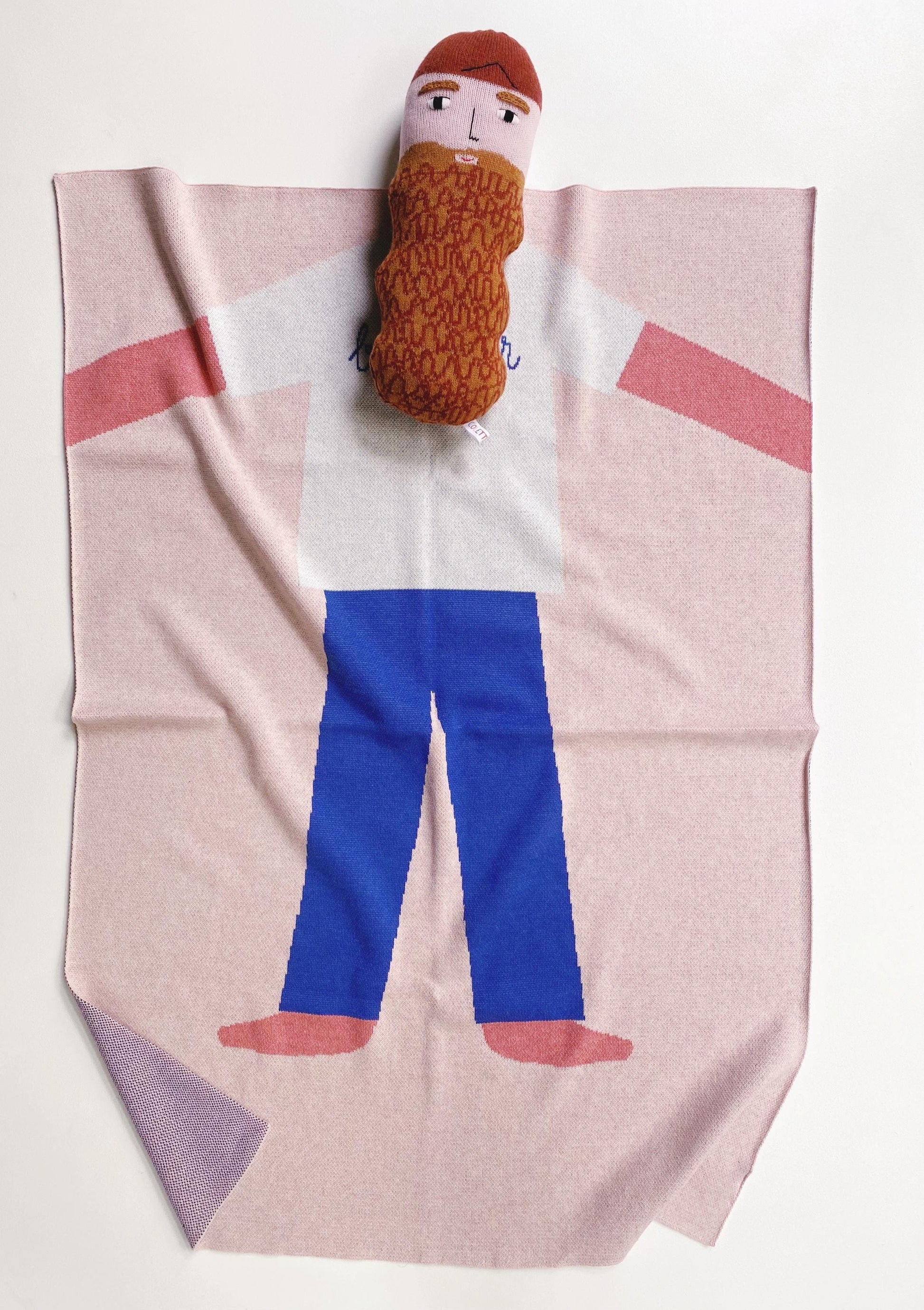 Knit baby blanket with a boy person character design featuring a plush toy doll om top