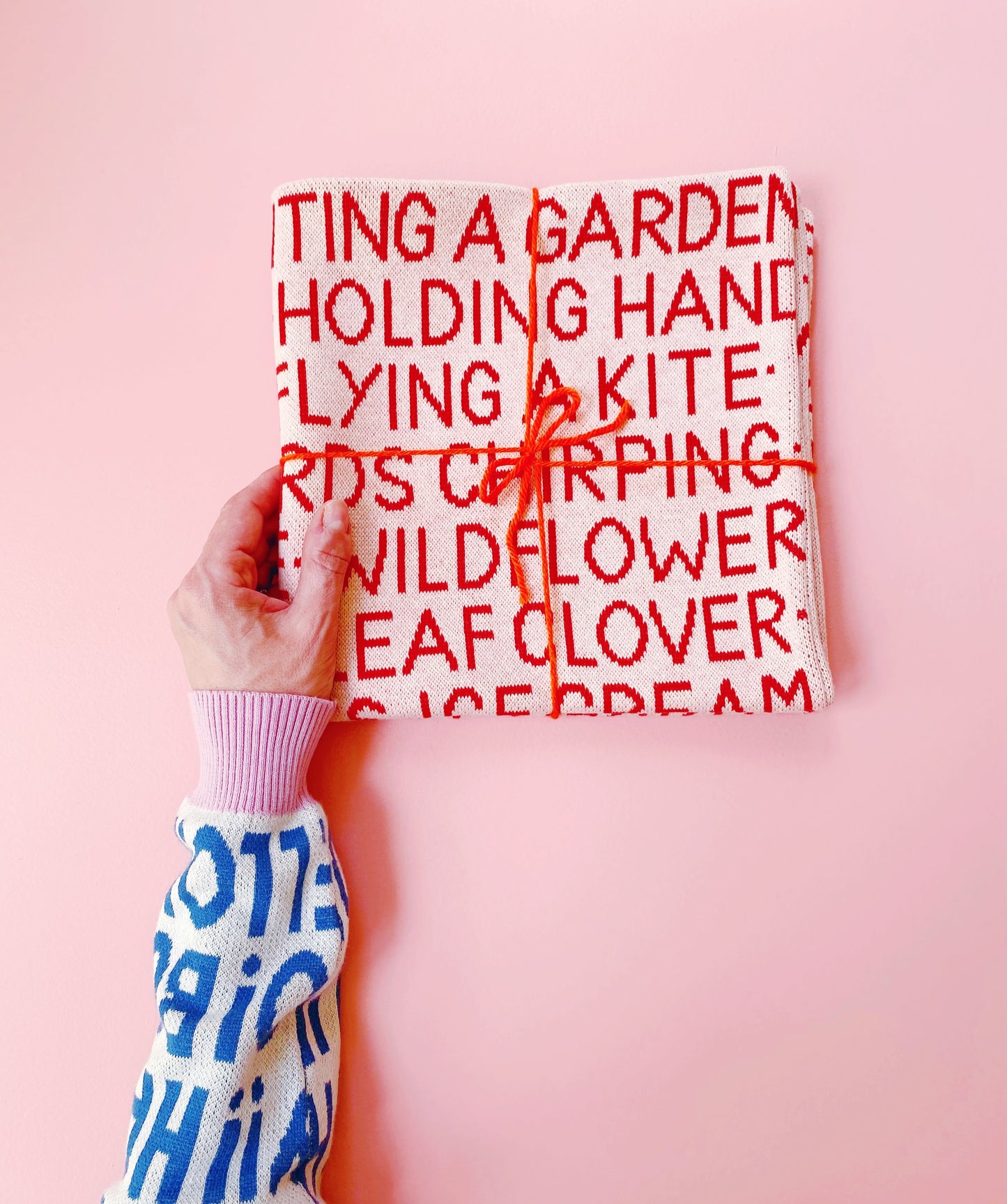Textured knitted Wordy pillow with red text on a pink background