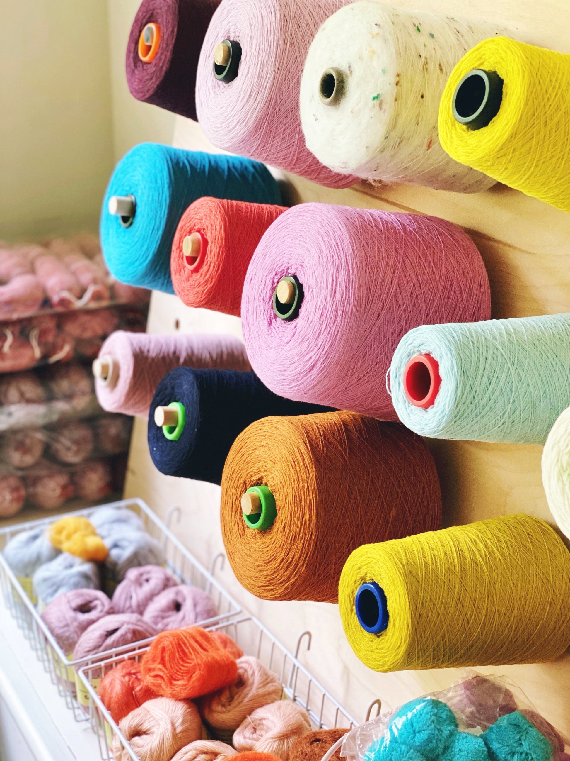 Colorful spools of yarn on a rack with a basket below.