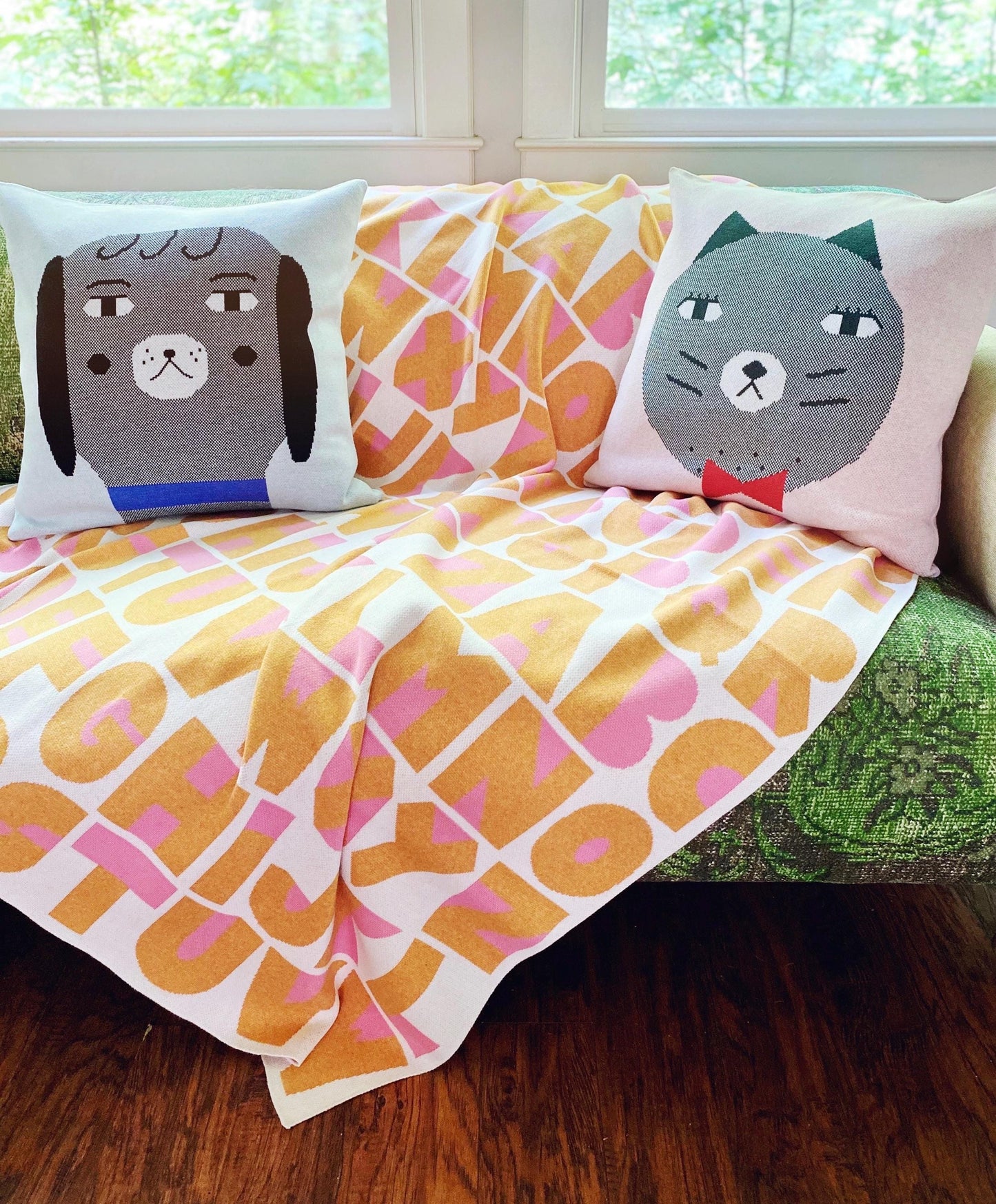 Sofa with patterned cushions and a colorful alphabet blanket in a room with windows.