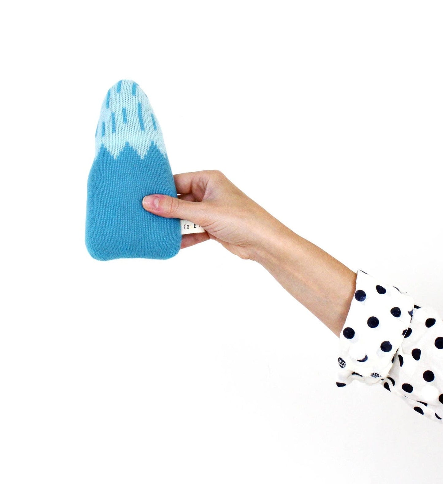 Hand holding a blue and white knitted mountain shaped baby rattle plush toy against a white background