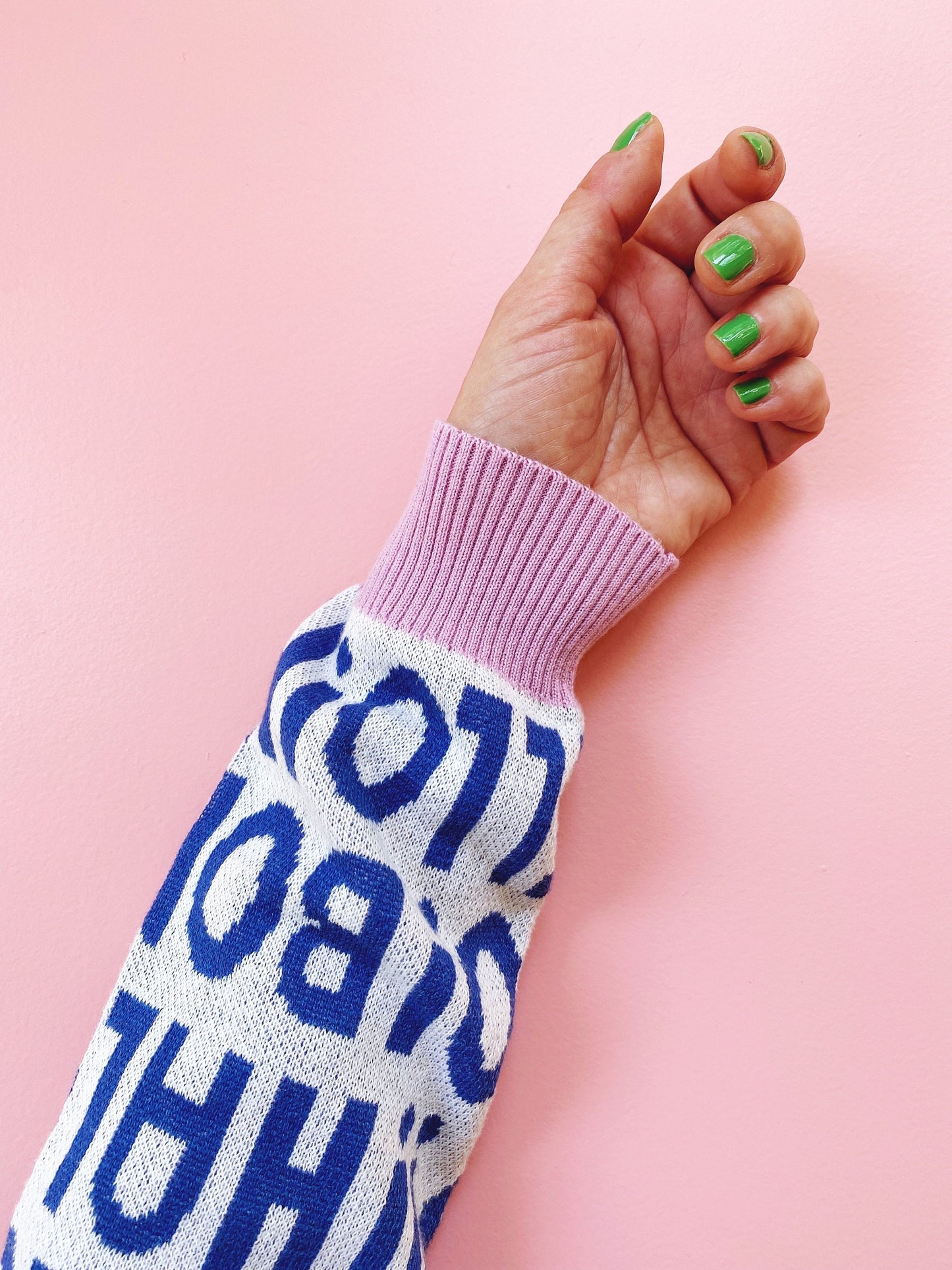 Hand in a sweater sleeve with blue text on a pink background