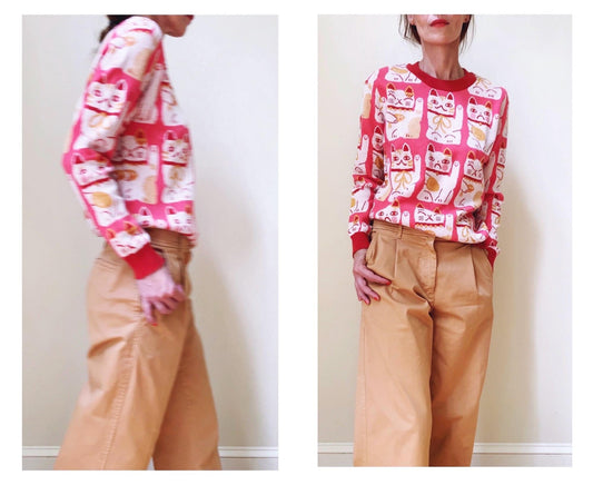 Two images of a person wearing a patterned maneki neko sweater and beige pants against a plain background.