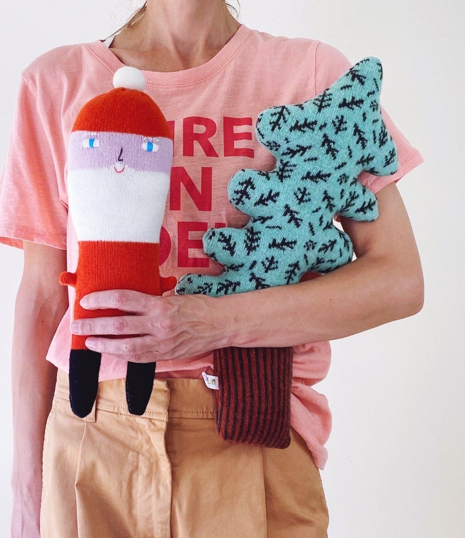 Person holding two plush toys, A Santa plush and a tree plush, against a white background