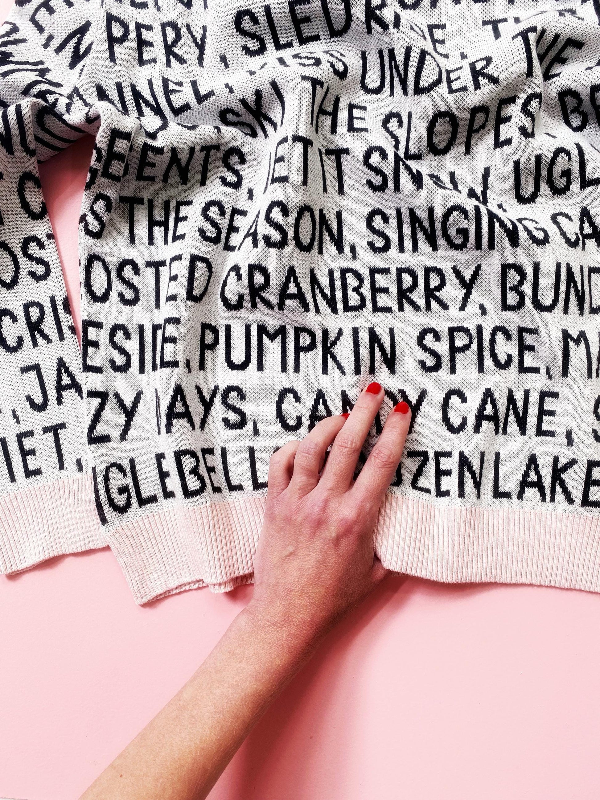 Knitted sweater showing textured fabric with black christmas festive text on a pink background
