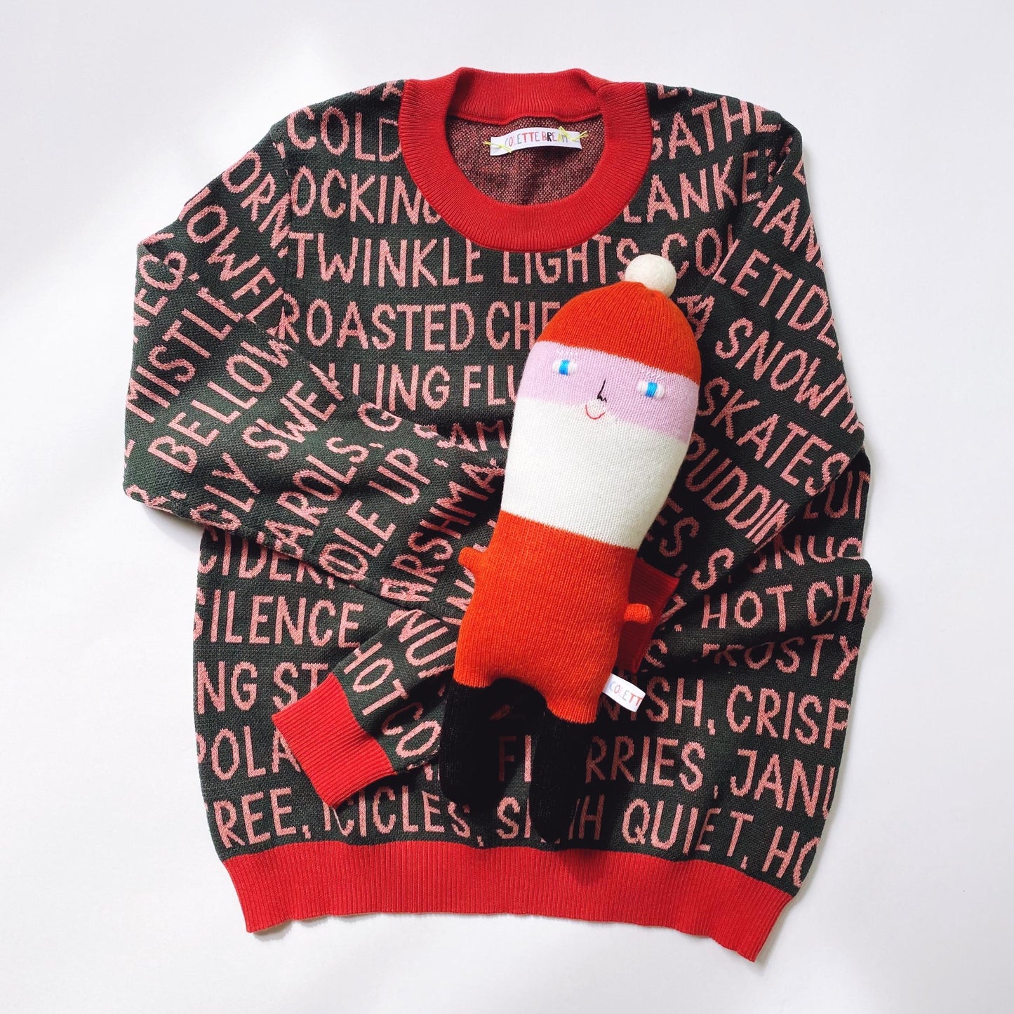 Knitted holiday sweater with a festive christmas text in pink and santa plush character on a white background