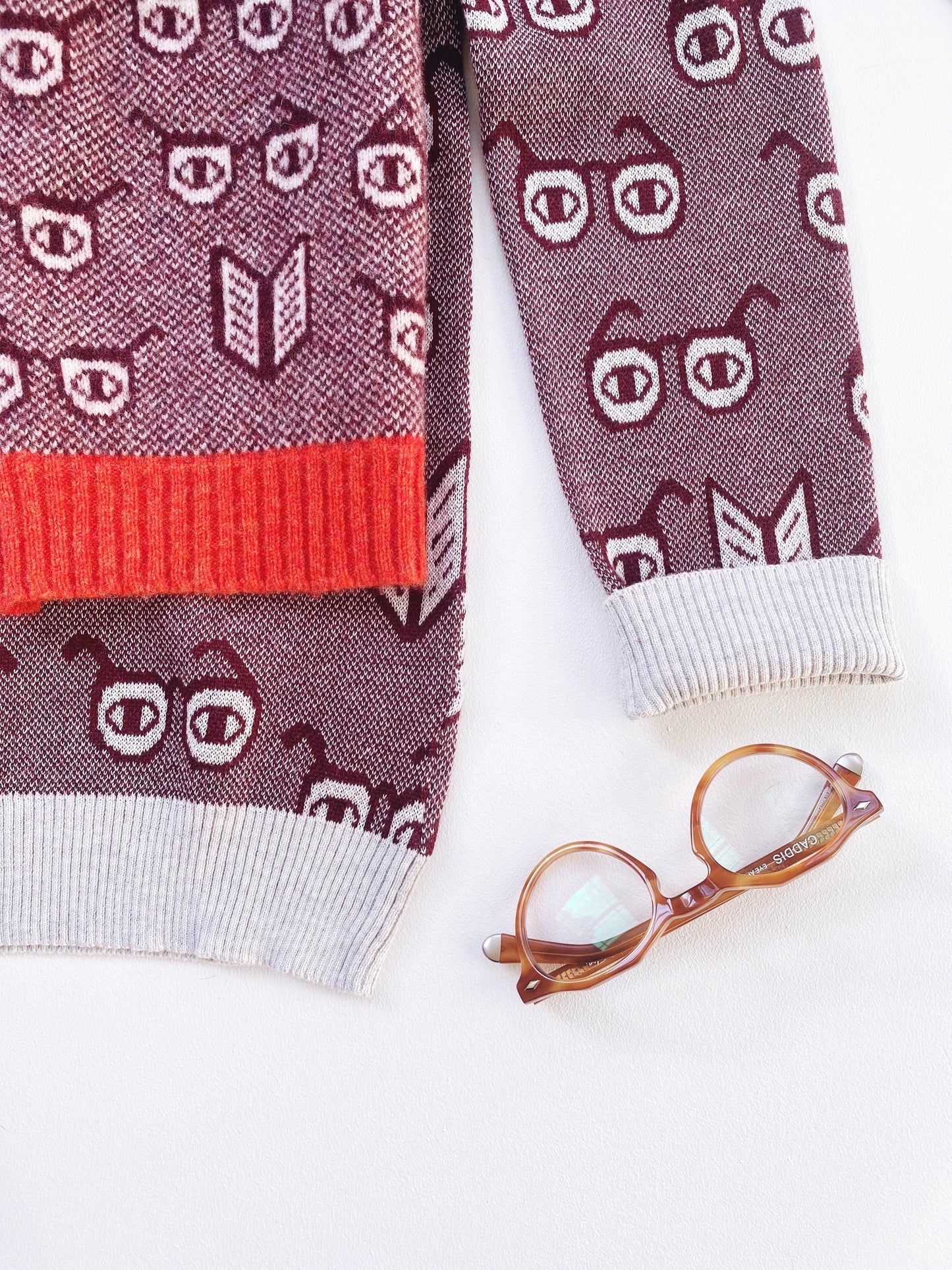 Sweater with spectacles eyeglasses themed pattern and a pair of glasses on a white background