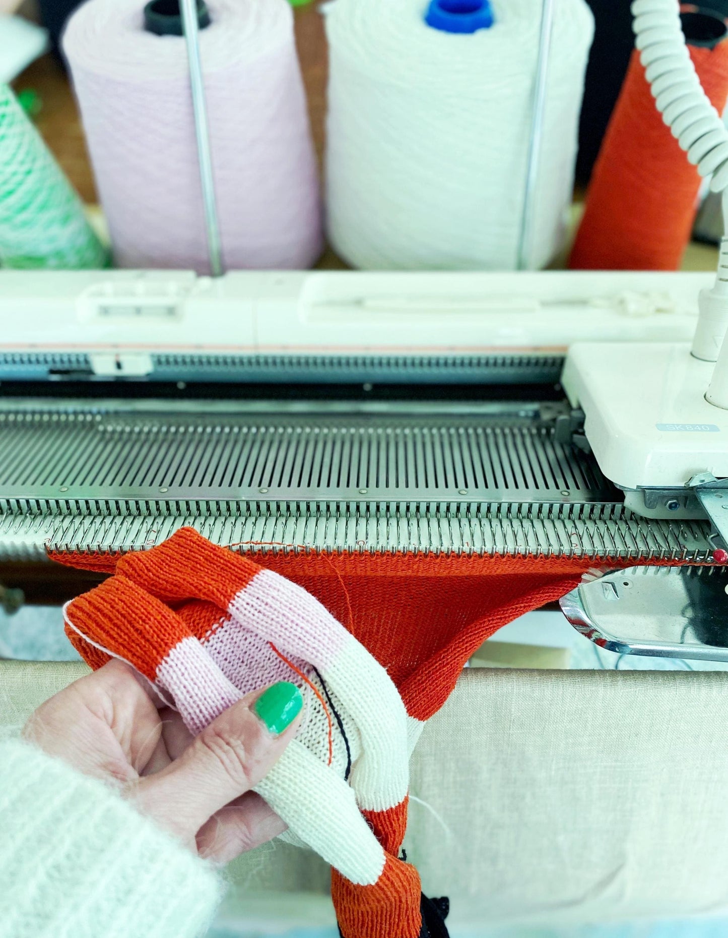 Knitted fabric with colorful pattern held by a hand next to a knitting machine.