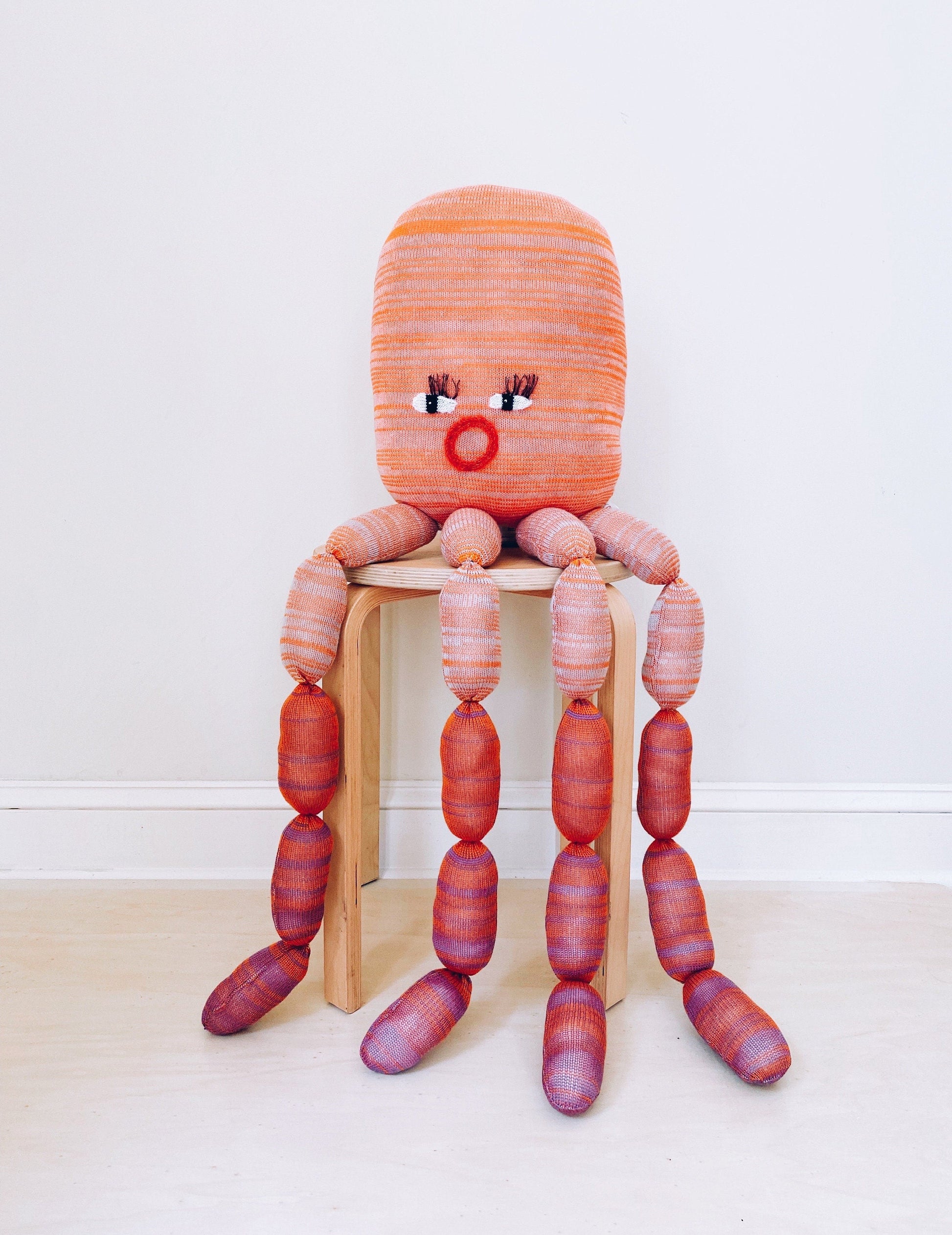 Large knitted Octopus plush toy with a striped design on a wooden stool against a white background