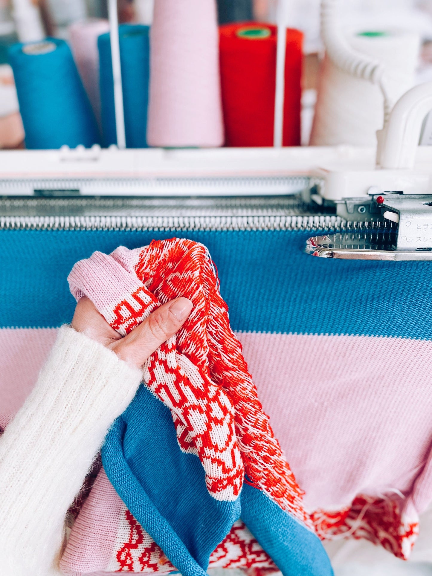 Person holding a knitted fabric with colorful yarn spools in the background