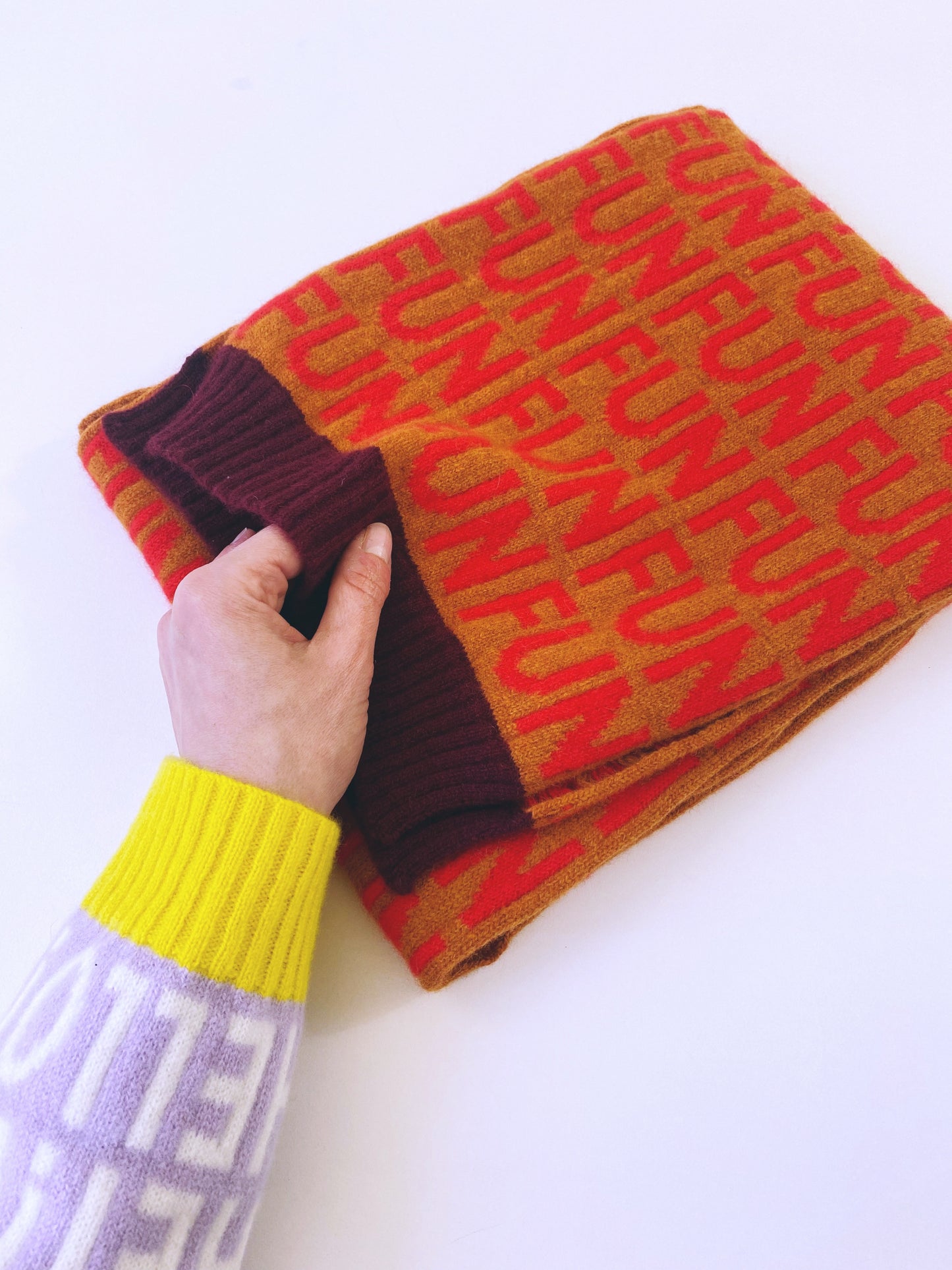Person holding a colorful knitted scarf with text on a white background