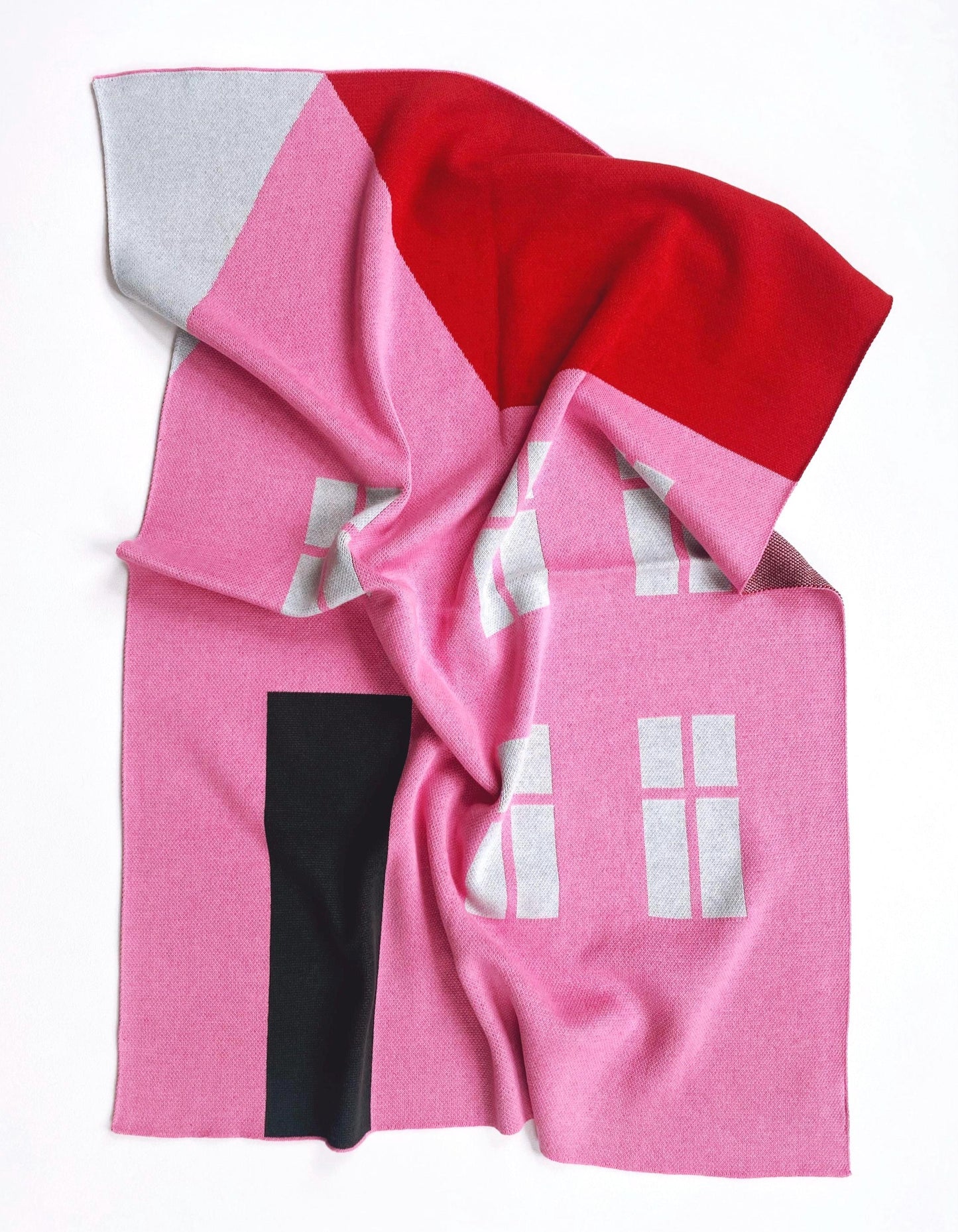 Pink knitted blanket with a house design on a white background