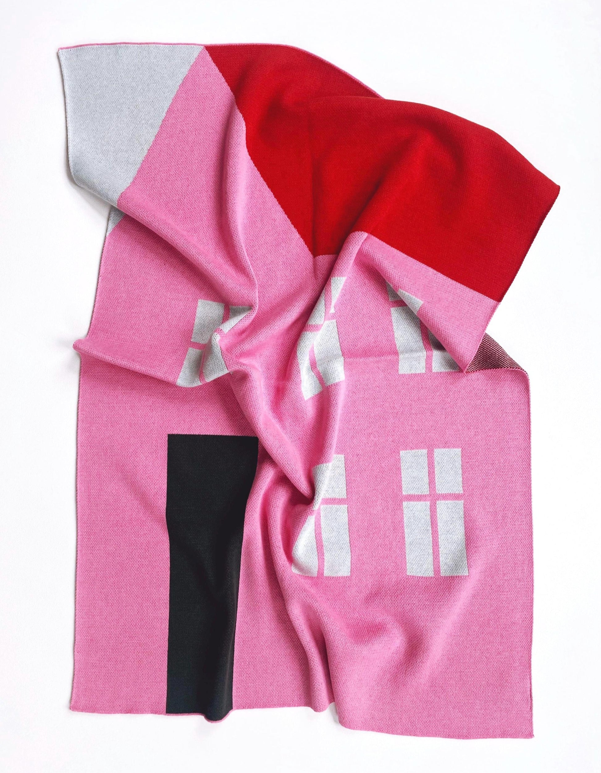 Pink knitted blanket with a house design on a white background