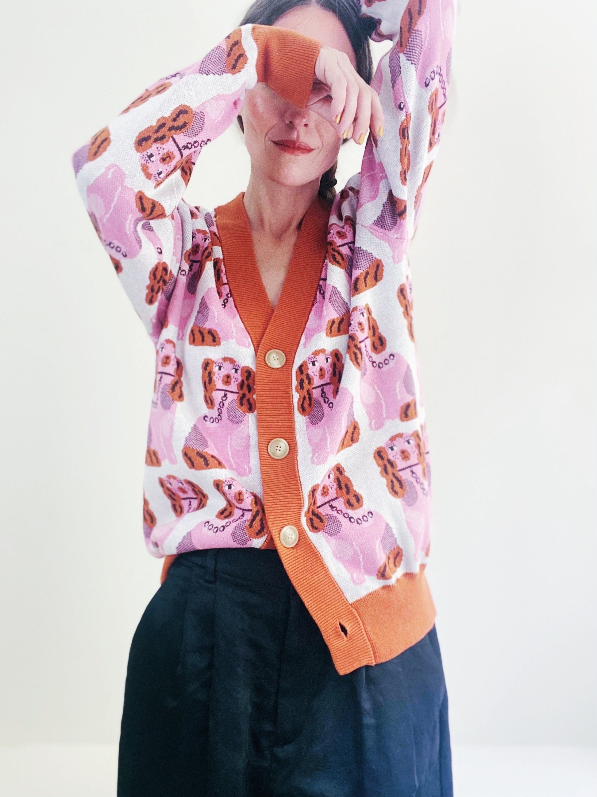 Person wearing a pink cardigan with staffordshire dog pattern and orange trim with buttons on a white background