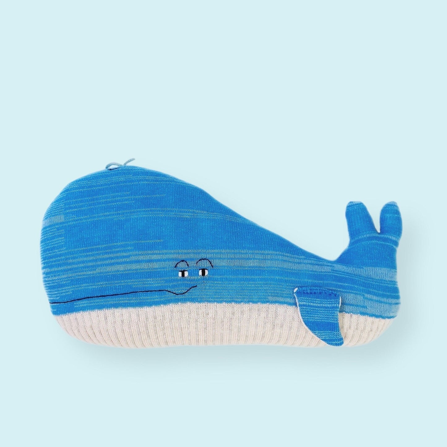 Blue knitted whale-shaped pillow on a light blue background